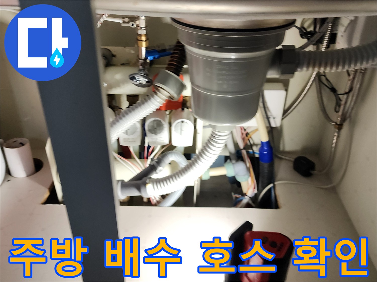 싱크대 하부장 내부의 굵은 배수 호스와 급수 밸브 연결 부위 근접 촬영