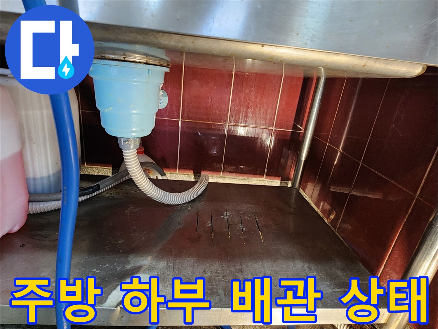 식당 주방 하부 배수구와 파란색 호스 및 스테인리스 선반 모습