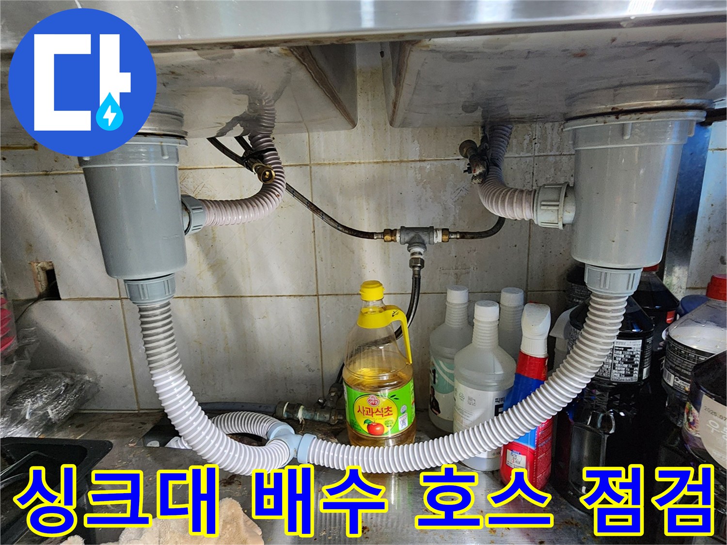 싱크대 하부의 회색 배수 호스와 연결 부속품들