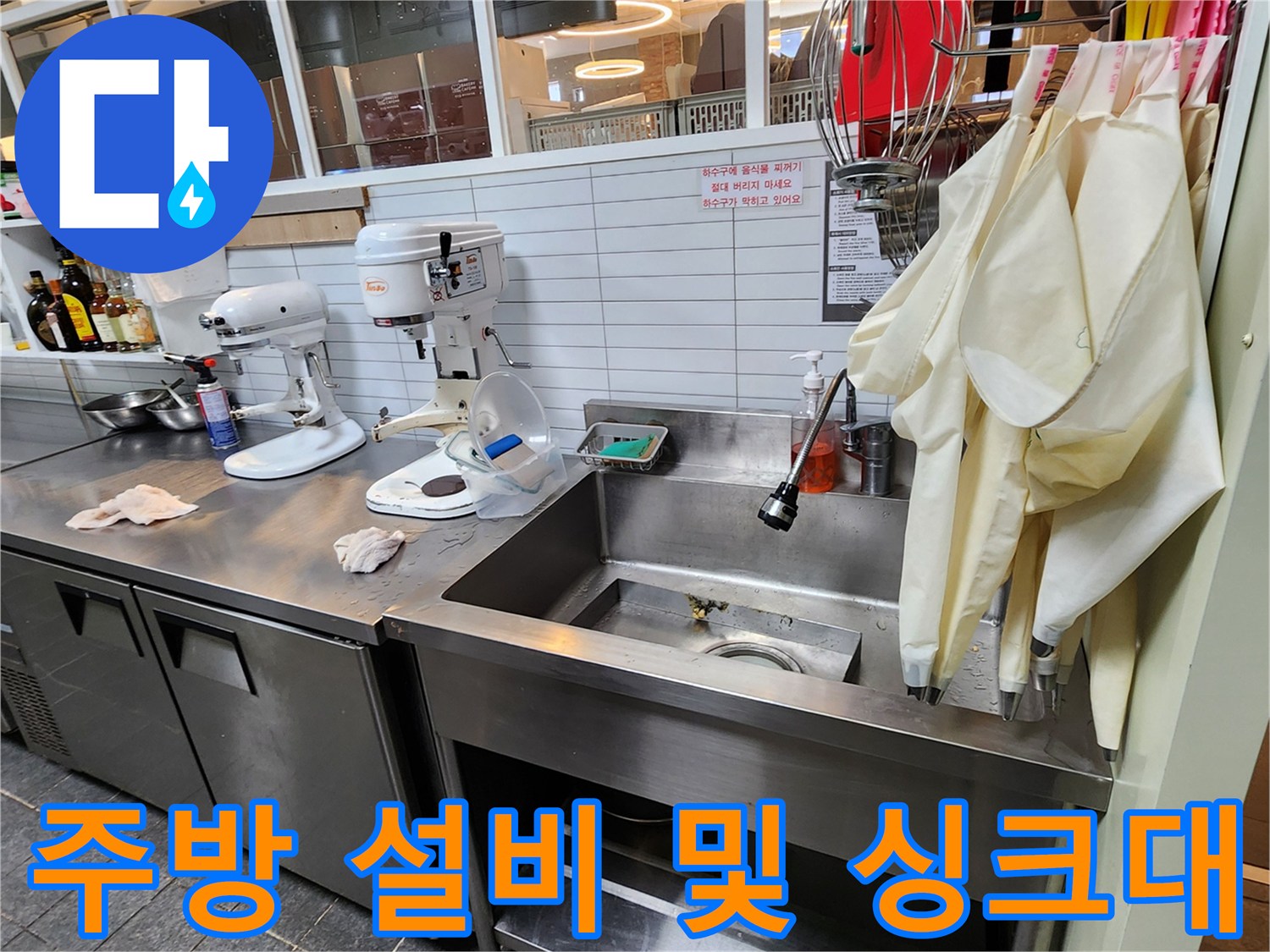 카페 조리 공간 내 배치된 스탠드 믹서와 스테인리스 싱크대 전경 - 누수 확인 작업 중
