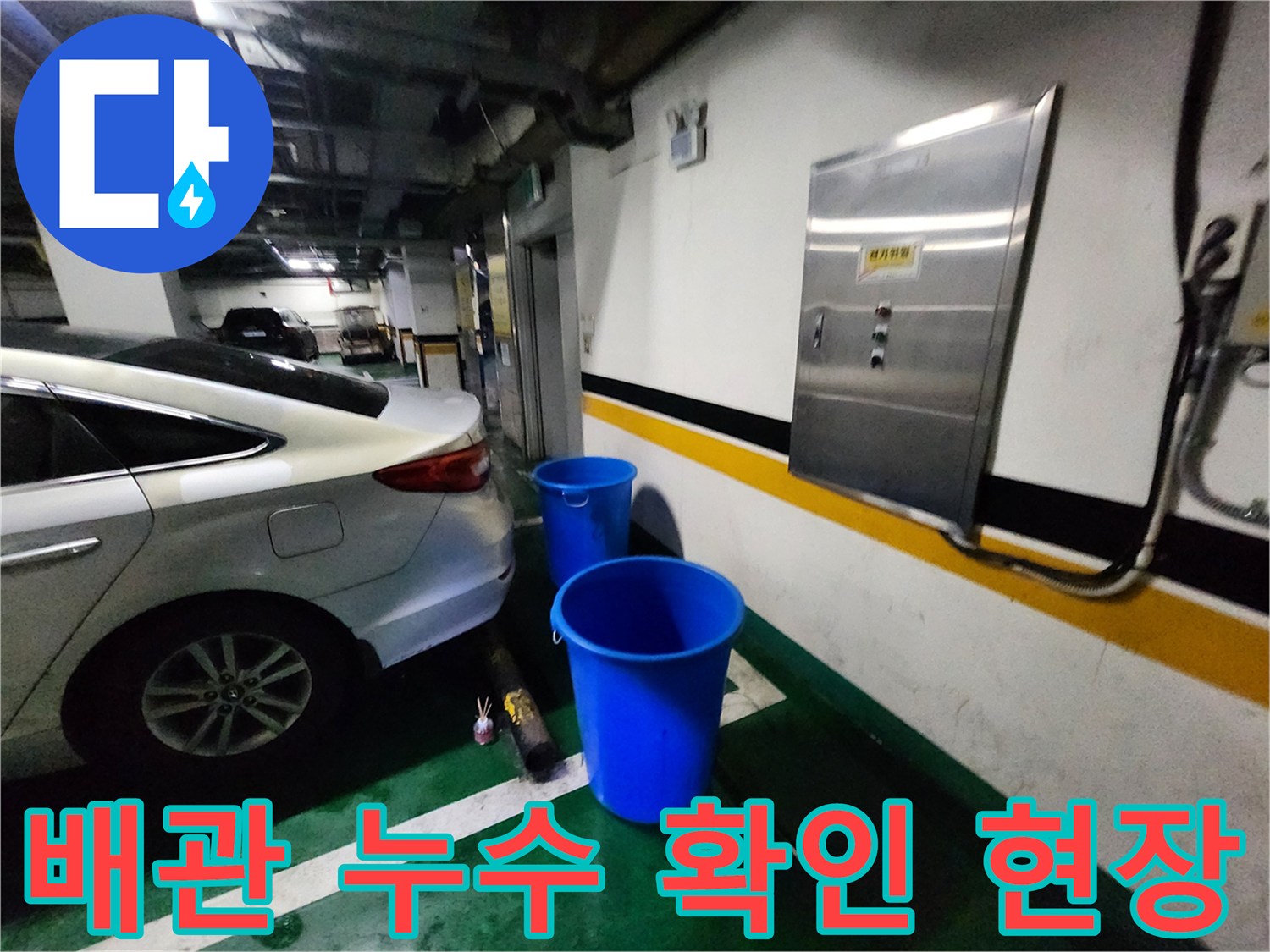 주차장 벽면 배전반 아래에 놓인 파란 양동이와 차량