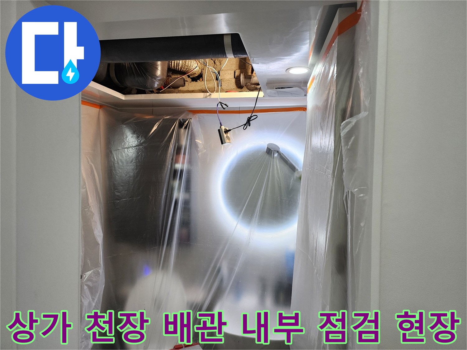 어두운 천장 속 배관 연결 부위를 조명으로 비추는 장면