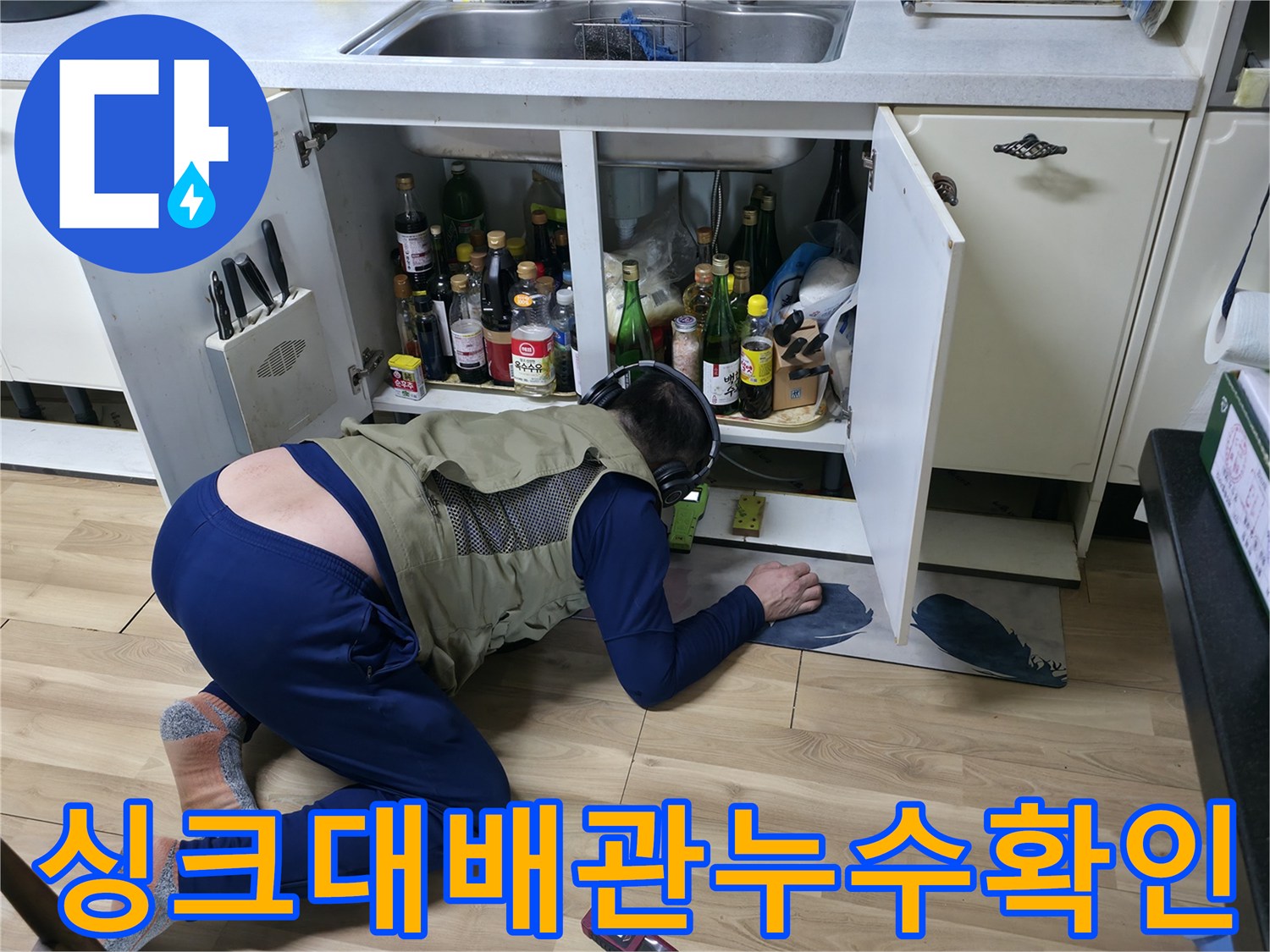 싱크대 아래쪽 좁은 공간에서 배관 누수를 면밀히 조사하고 있습니다.