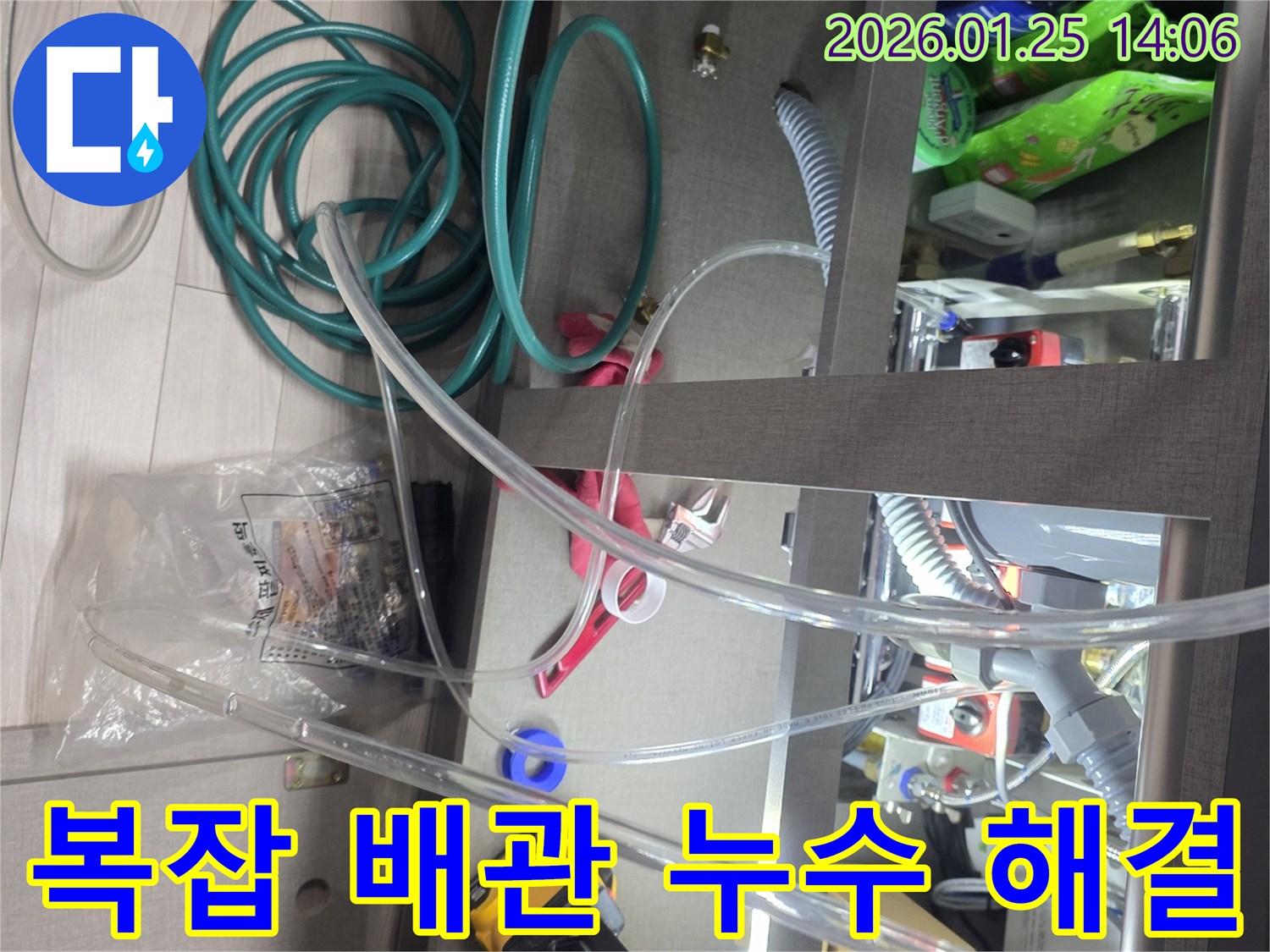 싱크대 하부의 복잡한 배관 구조 속에서-누수 지점을 찾아내고 해결하기 위한 준비 과정입니다-다양한 도구와 호스가 사용됩니다.