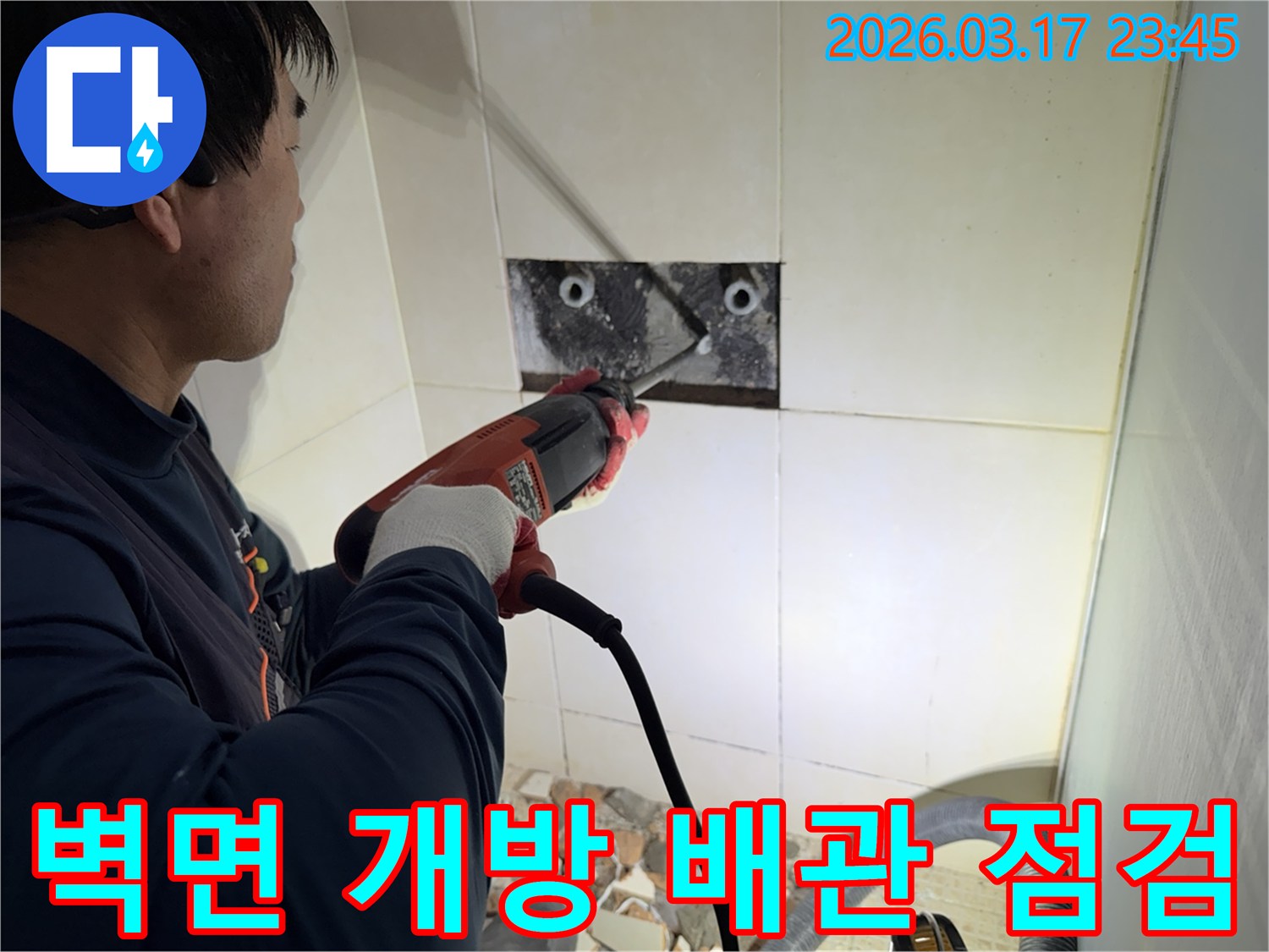 누수 공사 전문가가 주택 욕실 벽면의 타일을 조심스럽게 파쇄하여-누수 원인을 찾기 위한 배관 점검 작업을 진행하는 모습입니다.