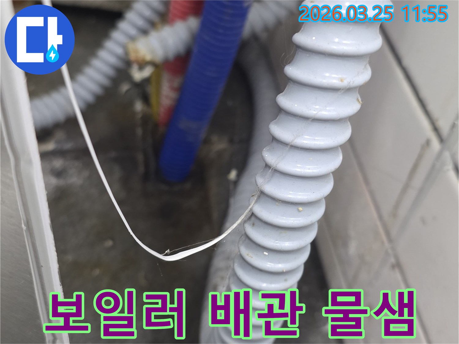 난방 또는 온수 공급을 위한-빨간색과 파란색 배관이-주름진 배수 호스 옆으로 지나가며-누수 가능성을 시사하는 모습