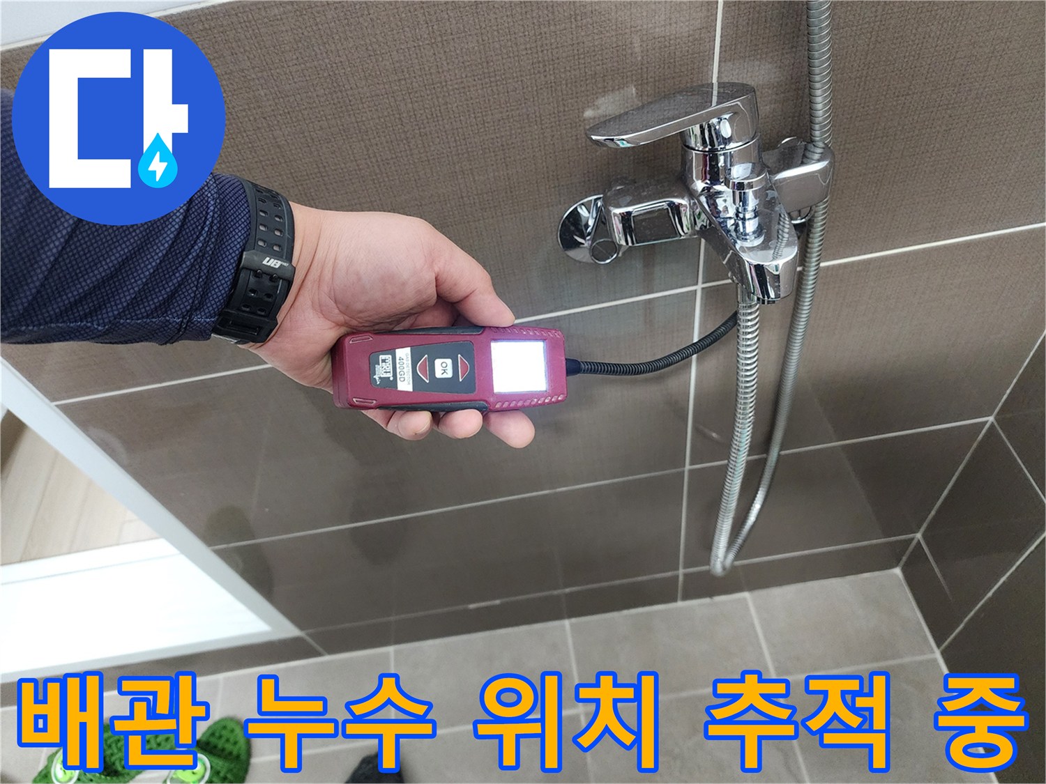 샤워 수전 배관에 연결된 휴대용 가스 탐지기를 사용하여 누수 지점을 찾는 장면입니다.