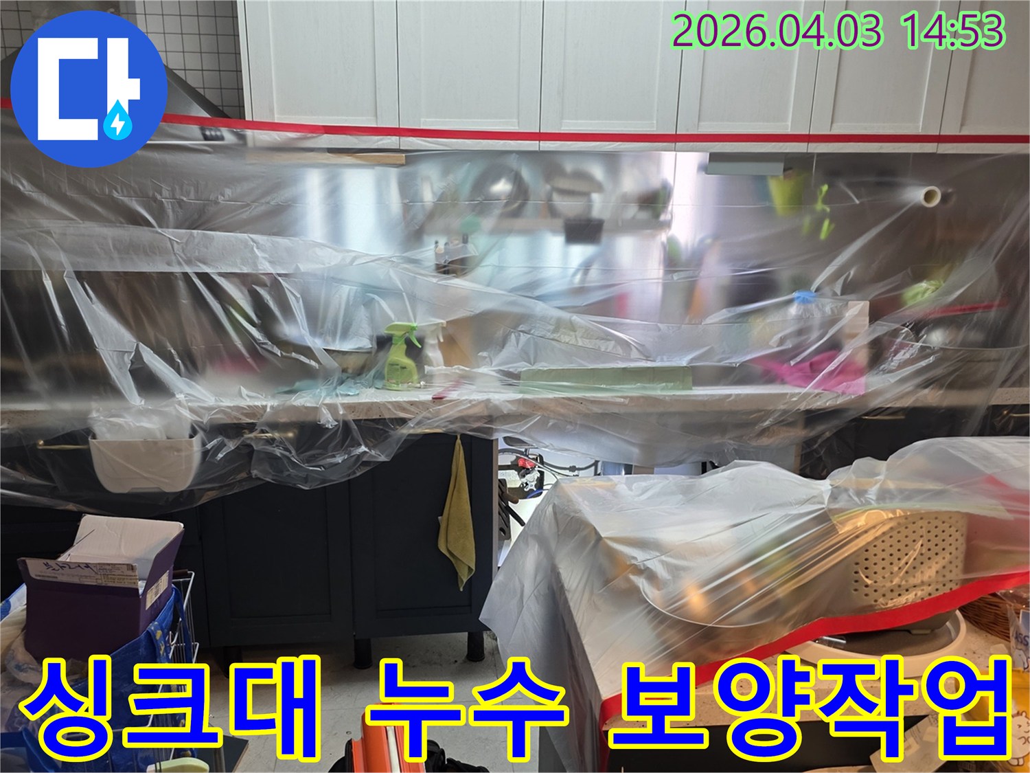 이 사진은 주방 싱크대 주변에서 발생한 누수를 해결하기 위해-작업 공간을 깨끗하게 유지하도록 비닐 보양을 마친 상태를 보여줍니다.