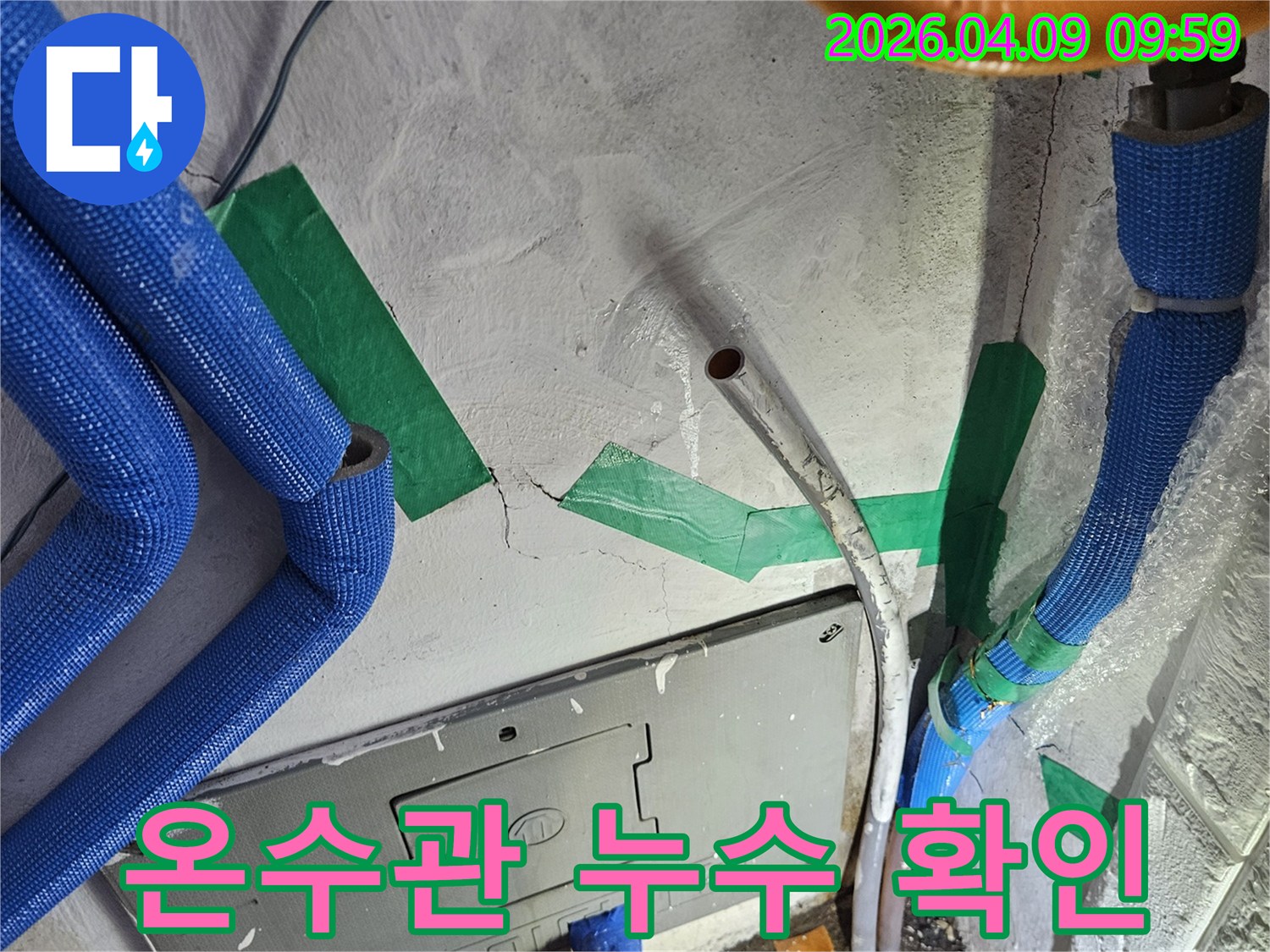 벽면의-콘크리트 균열과-파란색 보온재로 덮인-온수 배관-그리고 녹색 테이프로-표시된-누수 의심 지점의-상세 모습