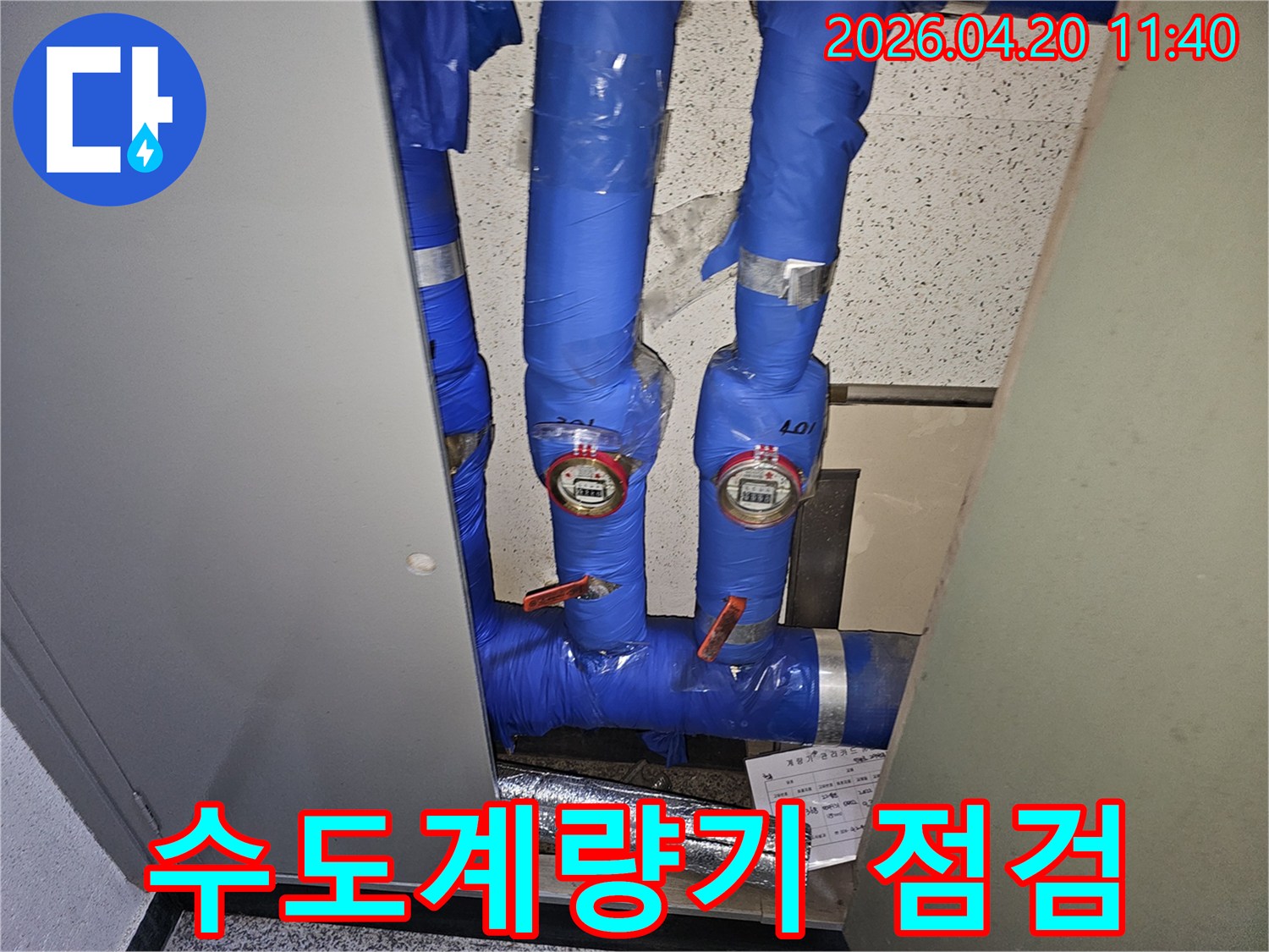 파란색 단열재로-감싸진-수도관과-두 개의-수도계량기가-보이는-누수-점검-현장-사진입니다.
