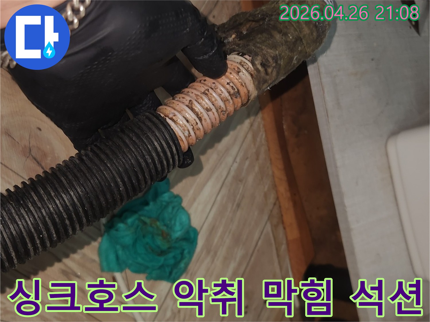 검은 장갑을 낀 기술자가-악취와 막힘의 원인인-오염된 싱크대 배수 호스를-석션 장비로 전문적으로 청소하는 중