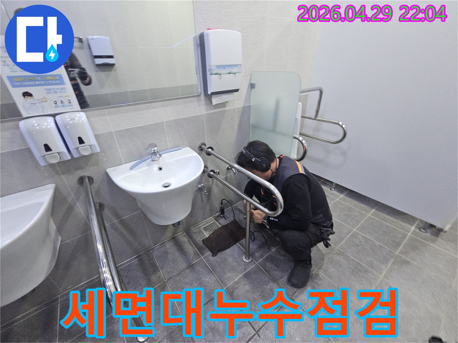 헤드폰을 착용한 기술자가-공용 화장실의 세면대 배관에서-미세한 누수 지점을 찾아내고 있습니다.
