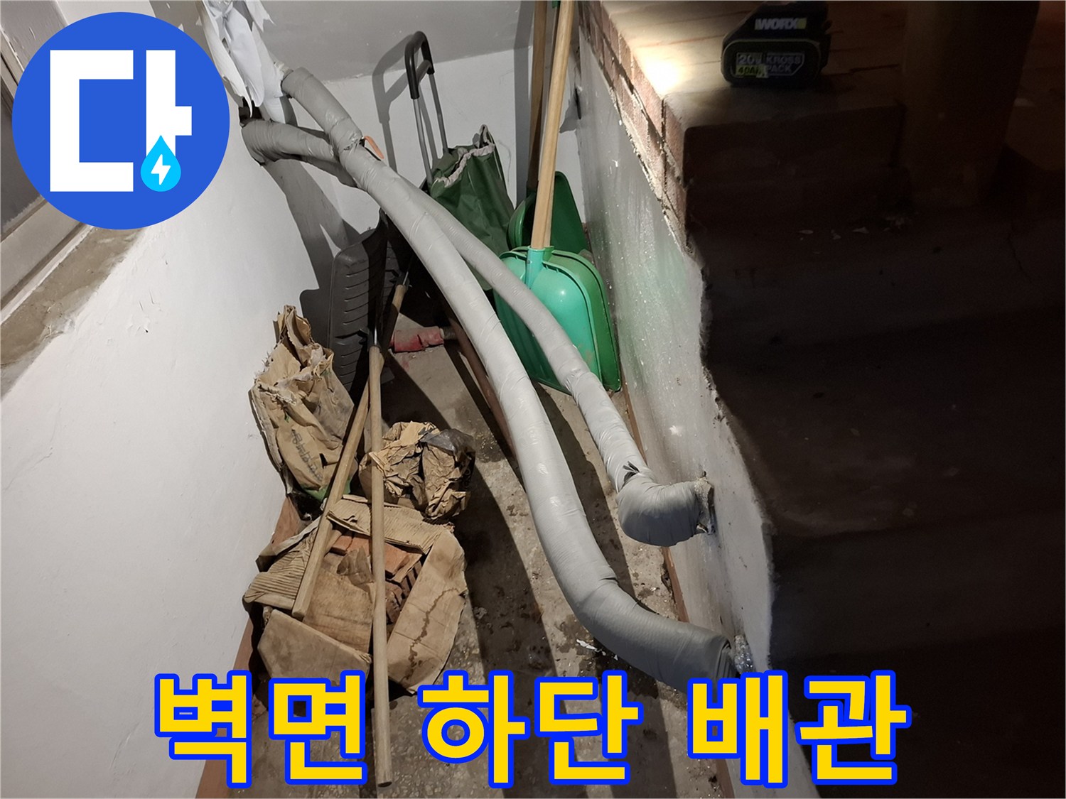 화장실-내부-벽면에-설치된-회색-배관과-청소용품