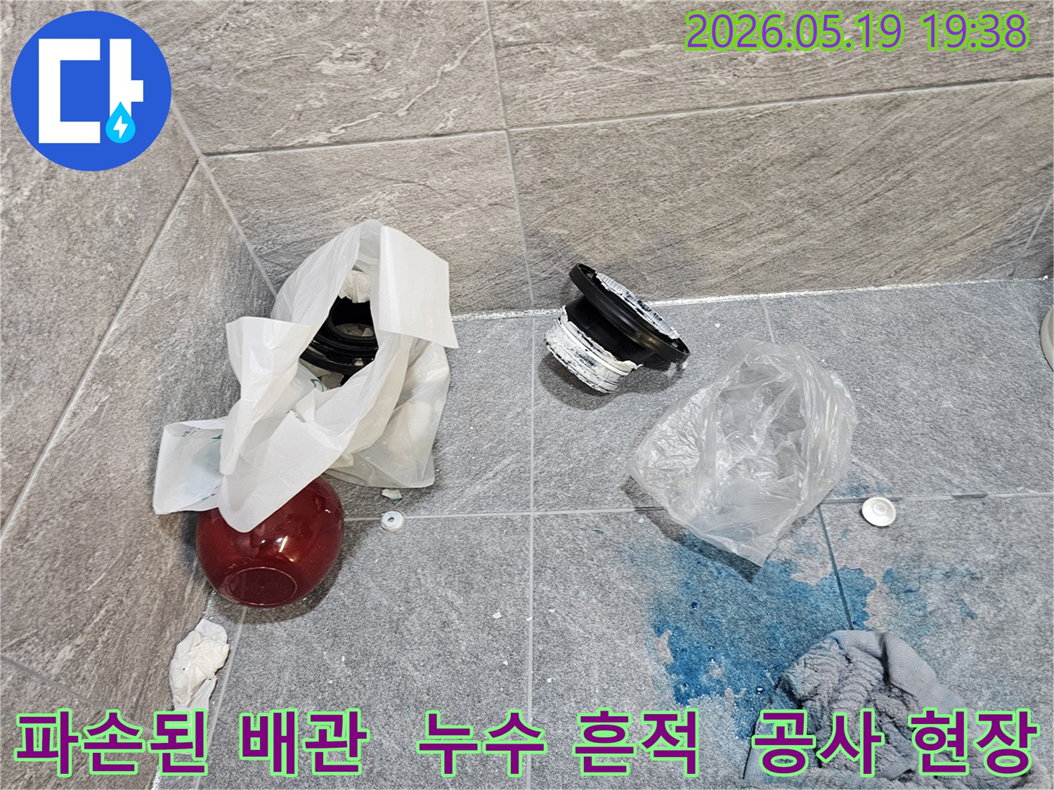 누수 공사 현장에서-파손된 배관 부품과-파란색 탐지액이 바닥에 흩어져 있는 모습입니다