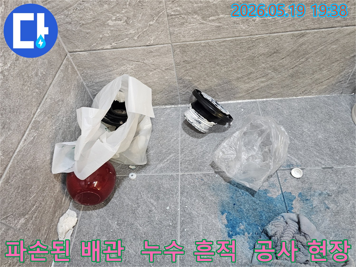 누수 공사 현장에서-파손된 배관 부품과-파란색 탐지액이 바닥에 흩어져 있는 모습입니다