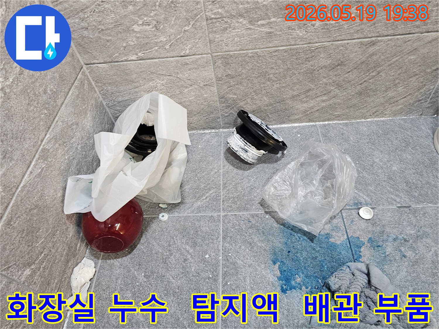화장실 누수 탐지 현장에서-파란색 탐지액이 누수 지점을 가리키고-주변에는 손상된 배관 부품들이 놓여 있습니다