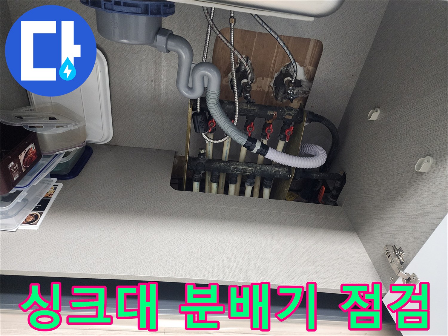 송파구 아파트-싱크대 하부장 내부의 보일러 분배기와 연결 배관 상태를 확인하는 모습