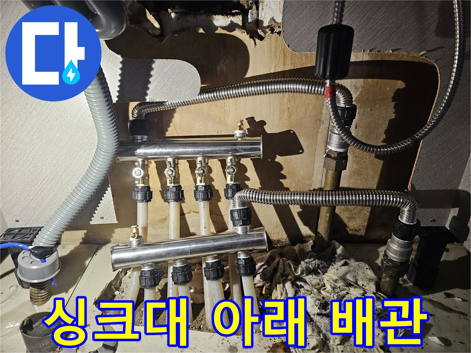 싱크대 하부장 내부의 은색 분배기와 스테인리스 관들