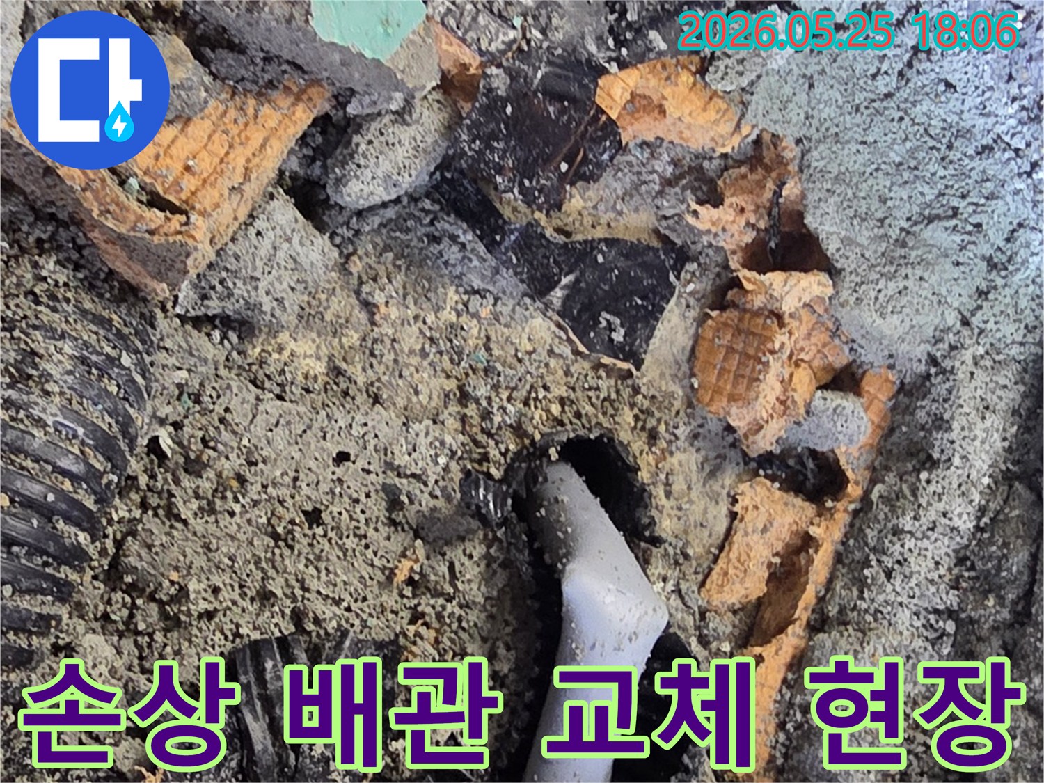 파쇄된 바닥 아래에서 발견된 낡은 배관과 주변의 젖은 흙-콘크리트 조각들이 누수 수리 과정의 한 단계를 보여줍니다.