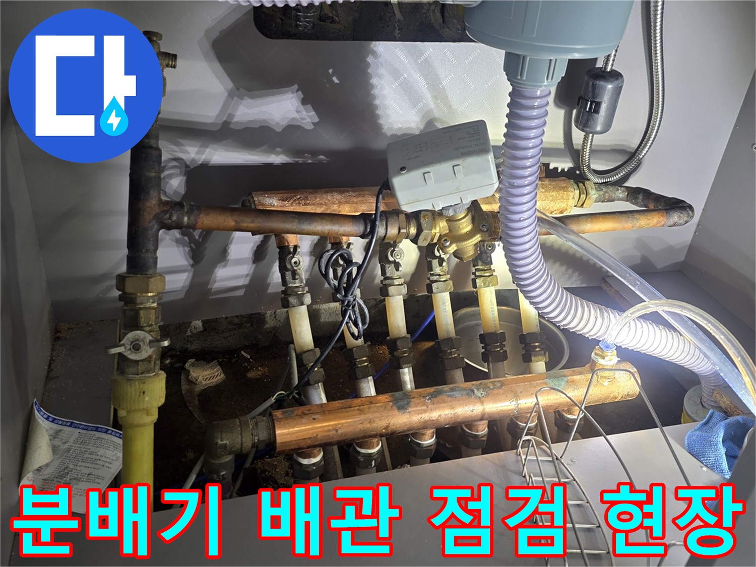 싱크대 하단 공간의 보일러 분배기와 다양한 연결 배관의 모습입니다.