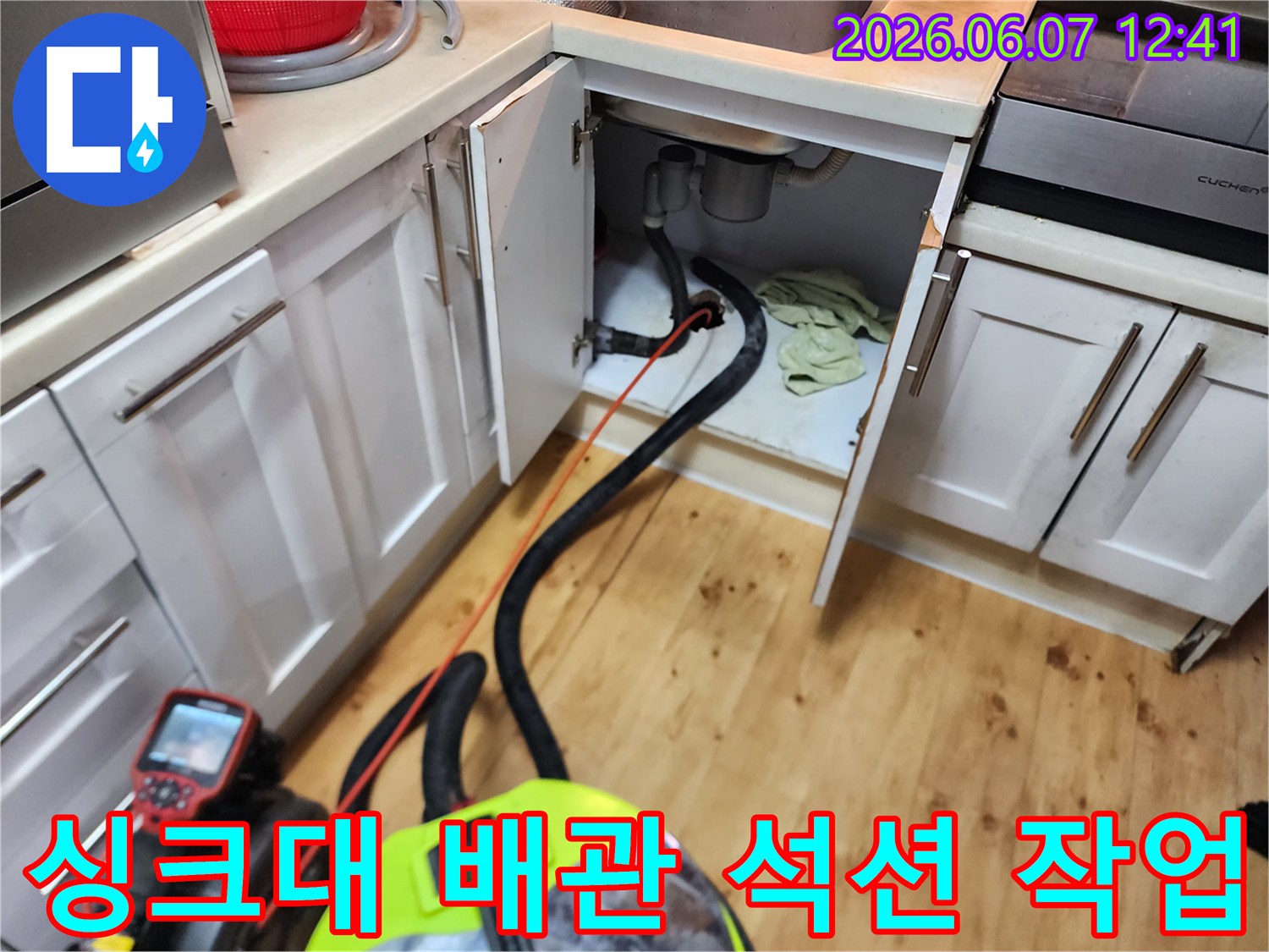 싱크대 하부장 내부 배관에 고인 물을 제거하기 위해 석션기를 사용하는 모습입니다.
