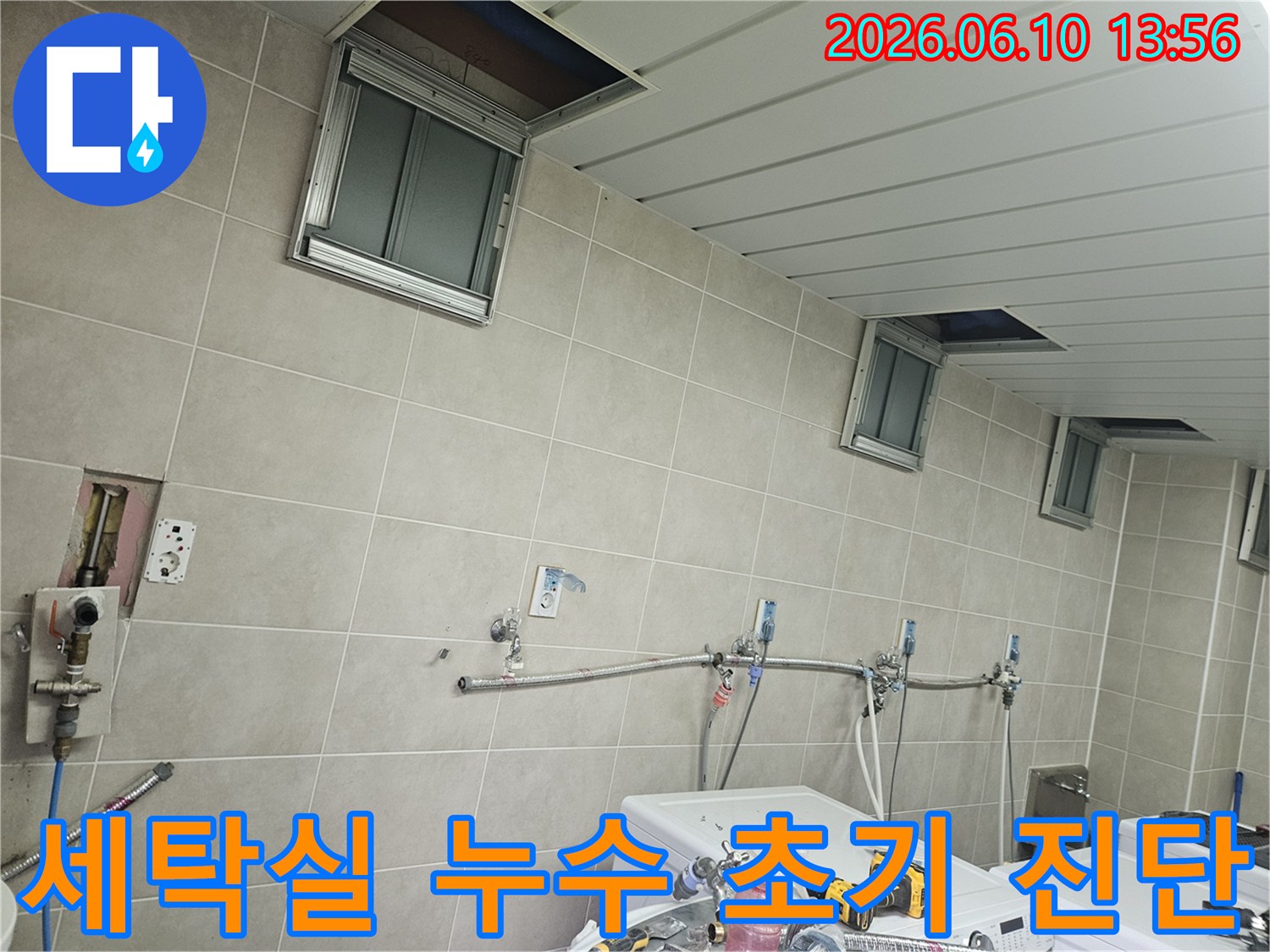 세탁기 옆 벽면의 수도 배관과 천장 점검구가 열린 채-누수 초기 진단에 집중하는-전문가의 모습