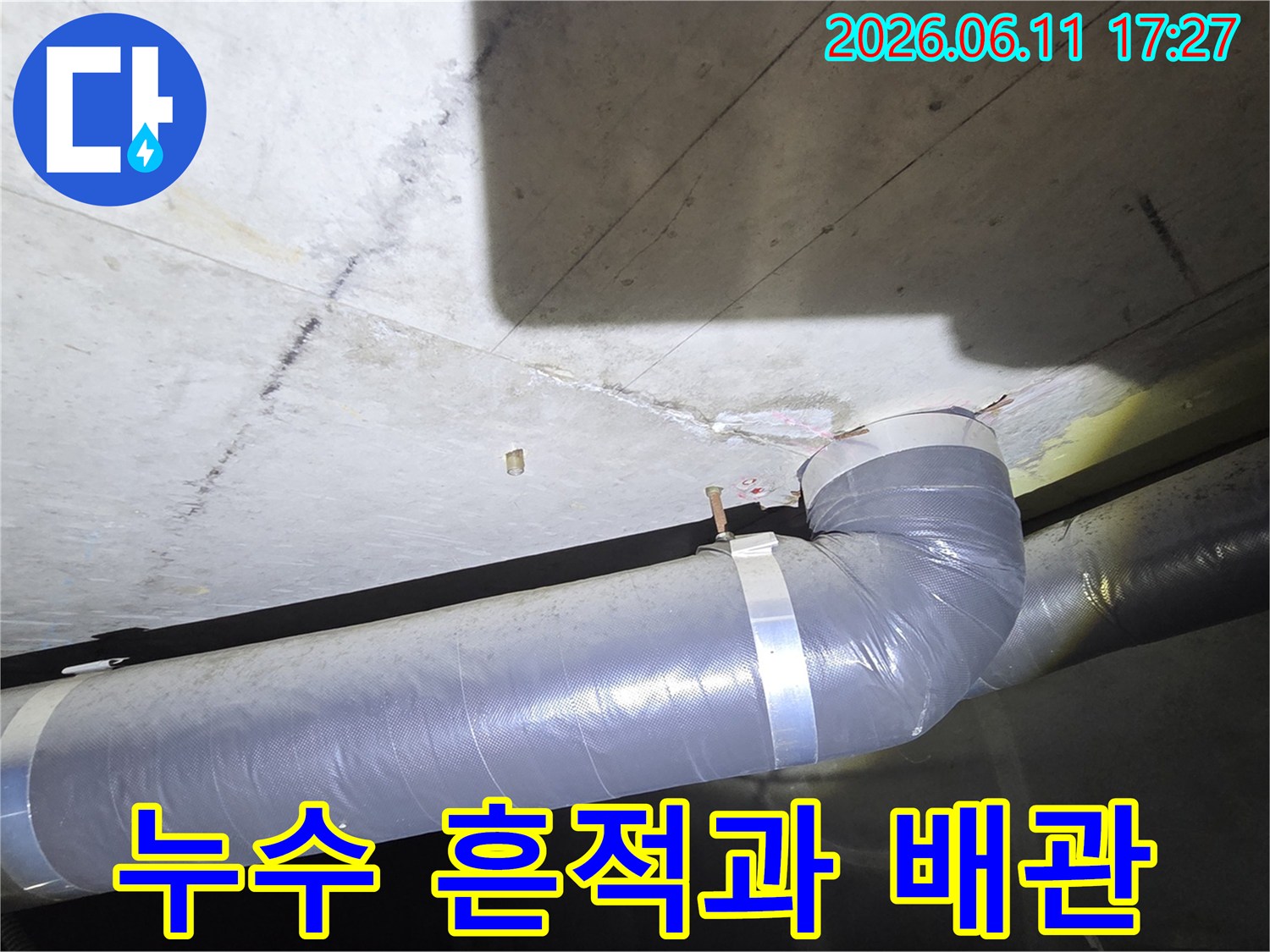 천장 콘크리트에 생긴 누수 얼룩과 그 아래로 지나가는 배관의 상태를 보여주는 근접 사진