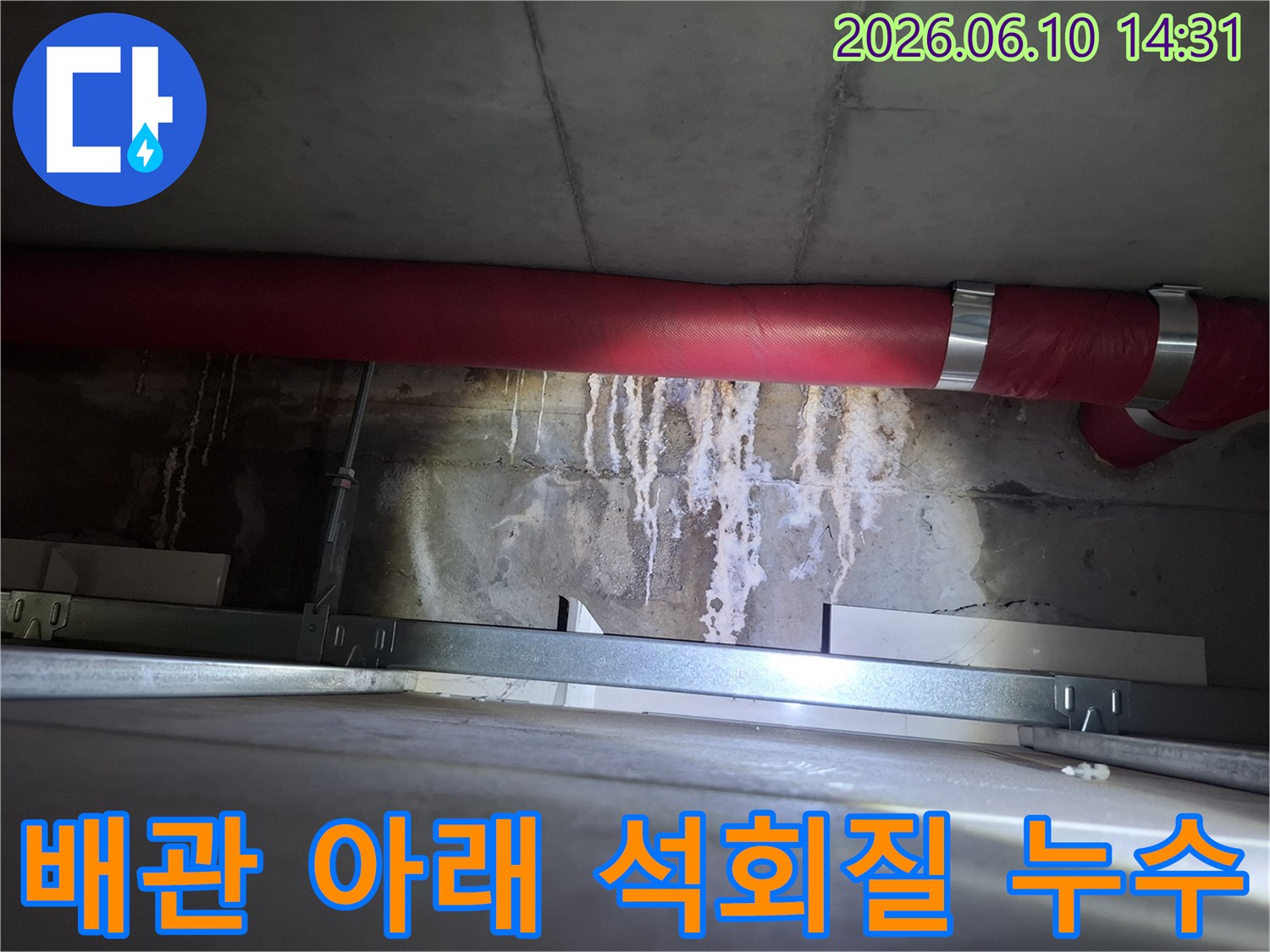 붉은색 배관 아래-콘크리트 벽면에 형성된-하얀 석회질 침전물과-누수 자국 이미지