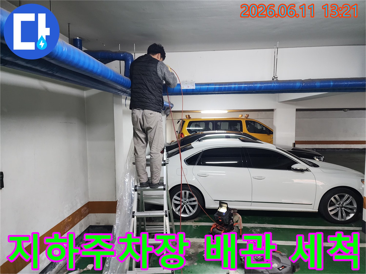 지하주차장 천장에 노출된 파란색 공용 배관을 고압 세척하는 모습입니다.