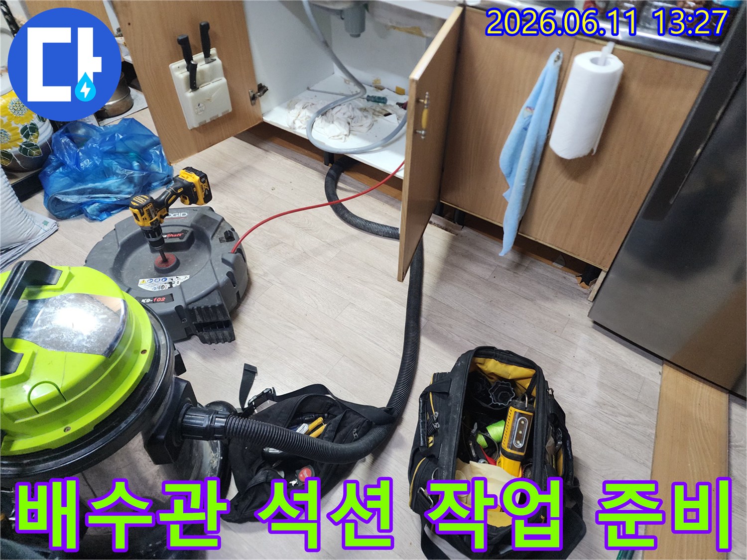 주방 싱크대 하단 배관 청소를 위해 석션기와 전동 공구를 배치한 모습
