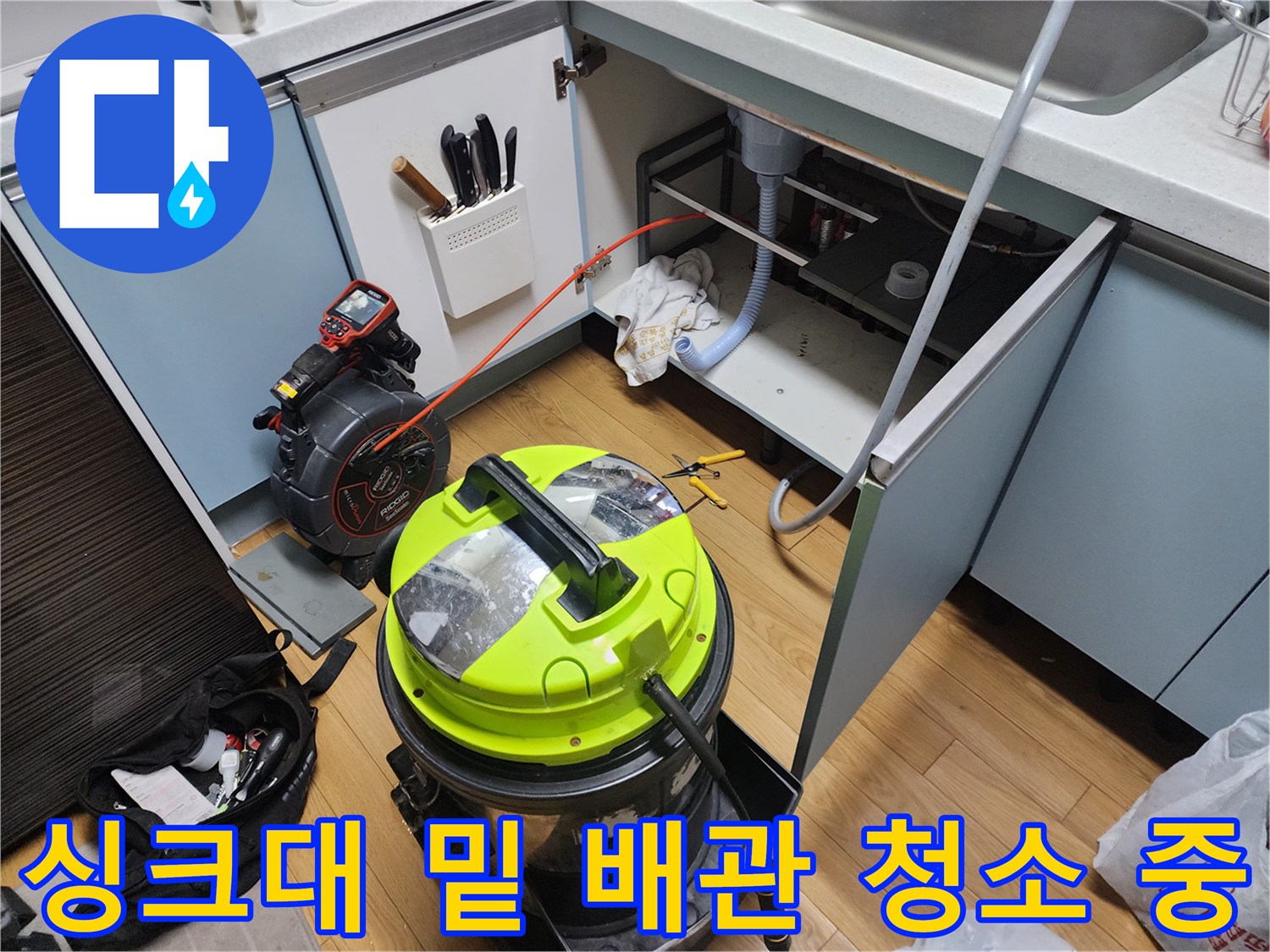싱크대 아래쪽 배관 주변에 배치된 전문 청소 장비와 공구들