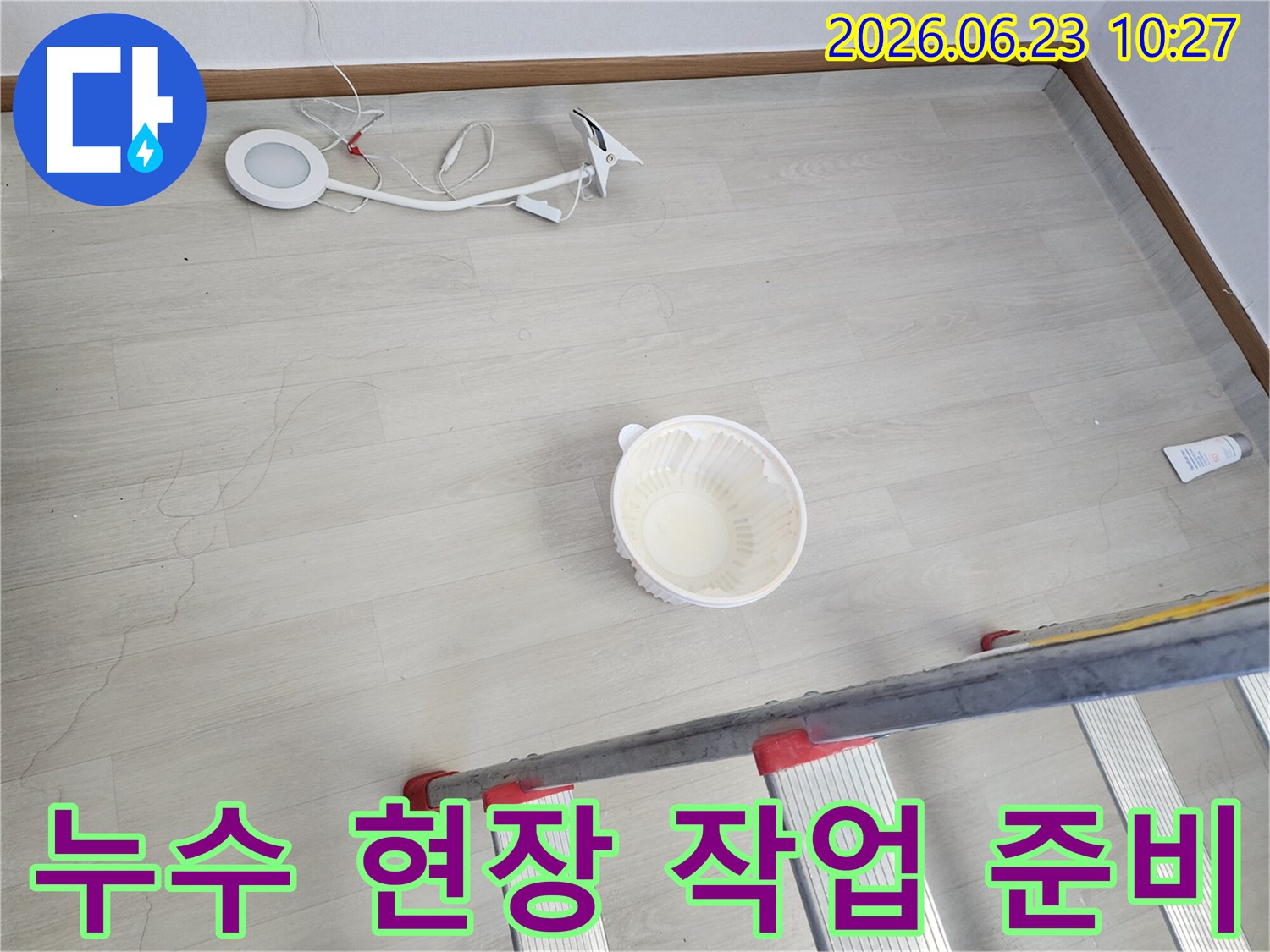 누수로 인해 바닥에 떨어진 물을 임시로 받는 그릇과-누수 지점 확인 및 수리를 위한 사다리-작업용 조명 장비가 바닥에 놓여 있는-누수 공사 전 현장 모습입니다
