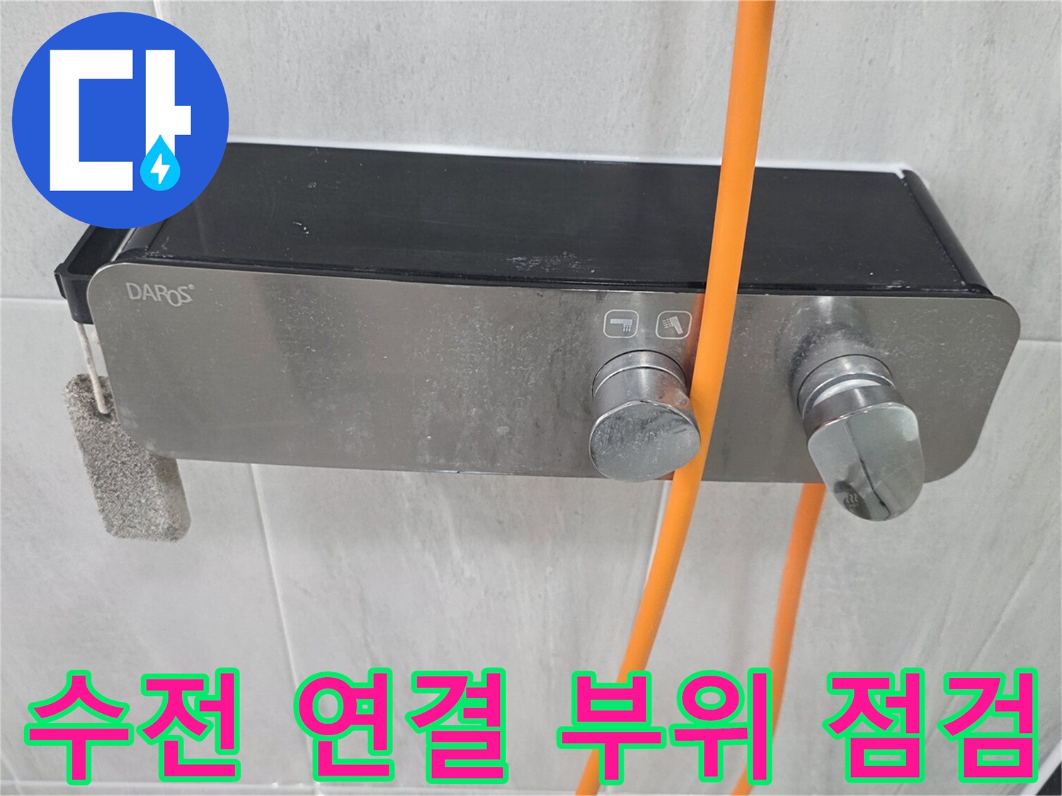 금속 수전과 주황색 호스가 벽면 타일에 설치된 모습