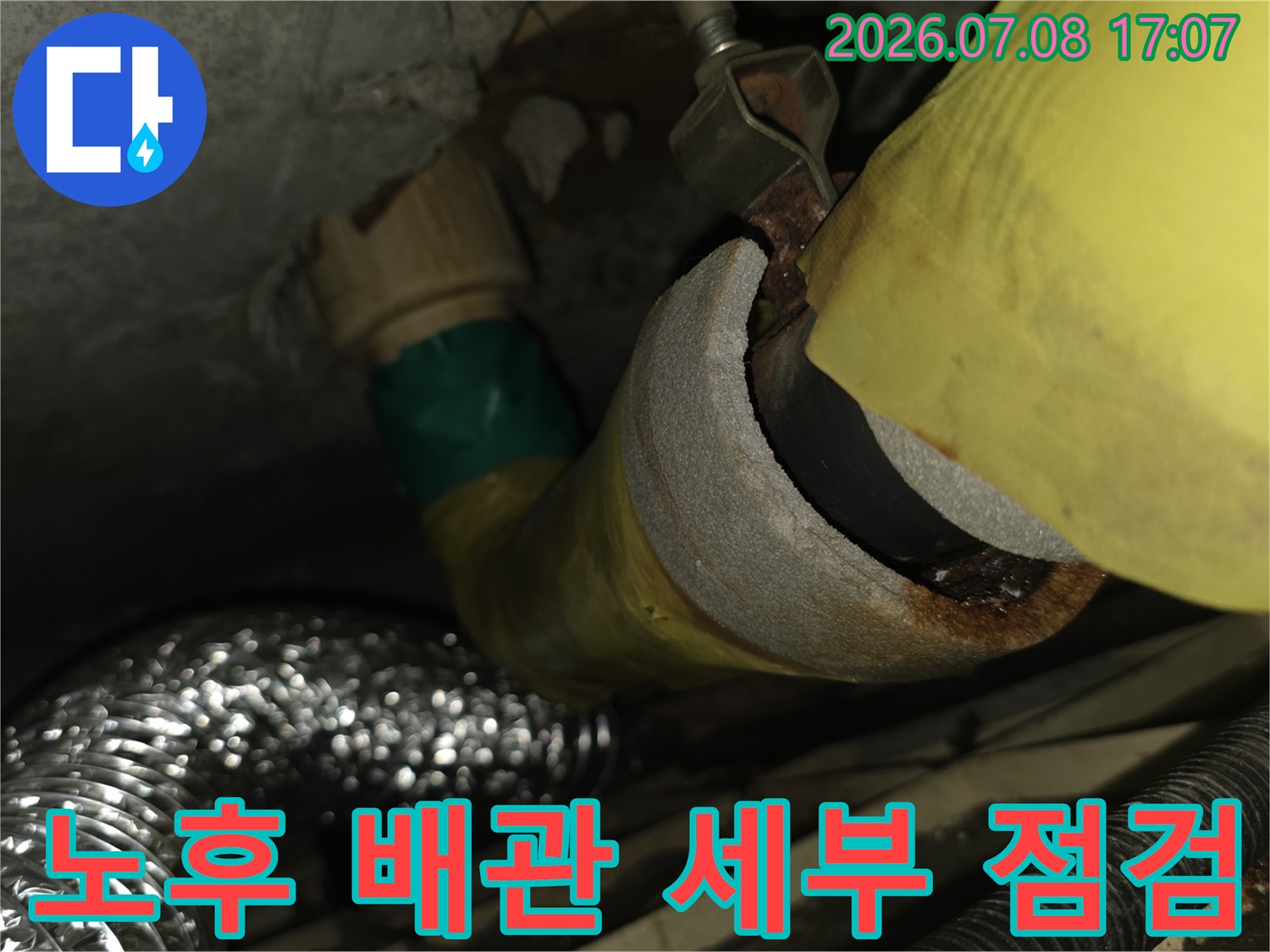 작업자가 수직으로 내려오는 배관의 연결 부위를 손으로 직접 만지며 상태를 확인하는 모습