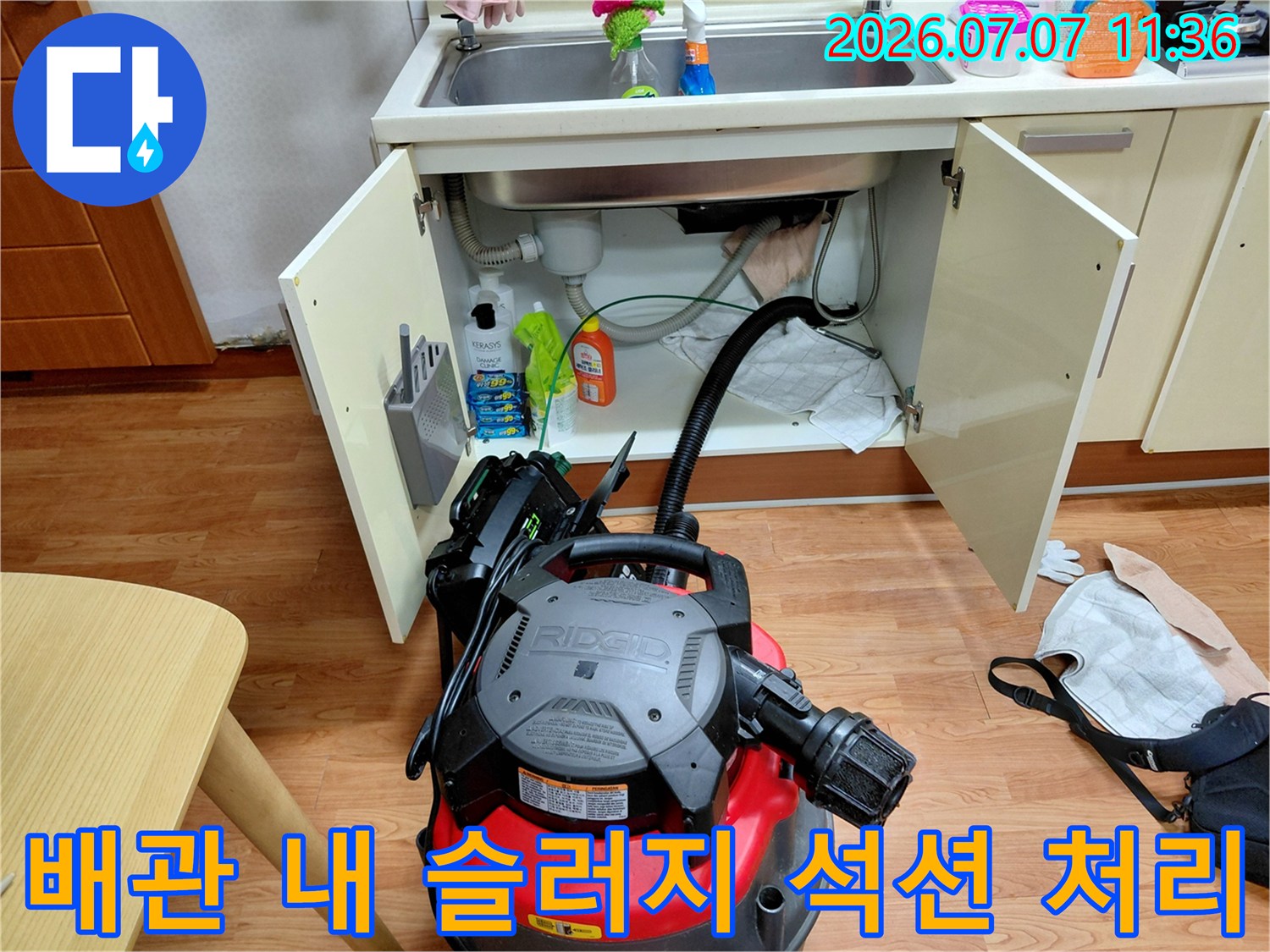 싱크대 하단부에서 전문 장비를 사용하여 배수구 내부 오물 제거 작업 중인 장면