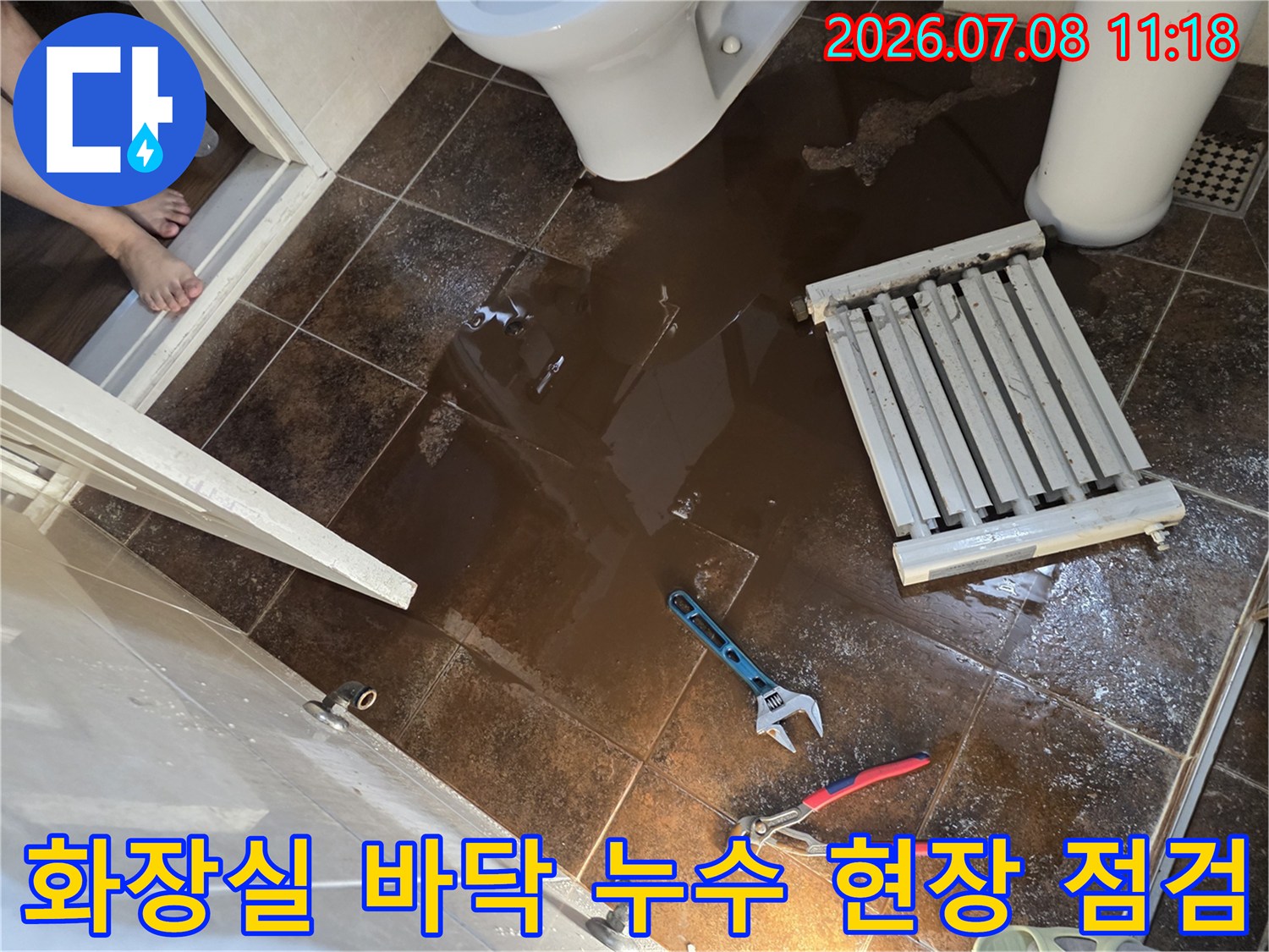 화장실 바닥에 물이 고여 있고 렌치와 라지에터가 놓인 누수 공사 현장