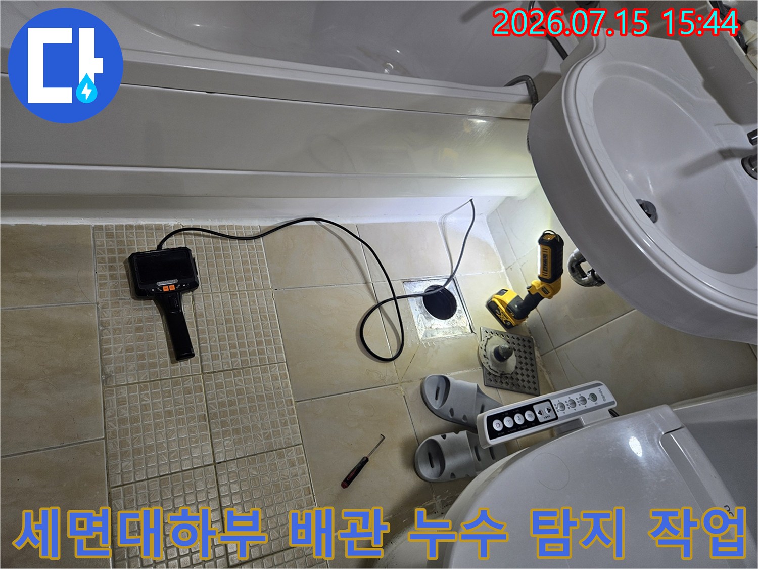 세면대 아래쪽에서 청음식 탐지기와 전동 드릴을 사용하여 배관 누수 지점을 정밀하게 찾아내는 장면