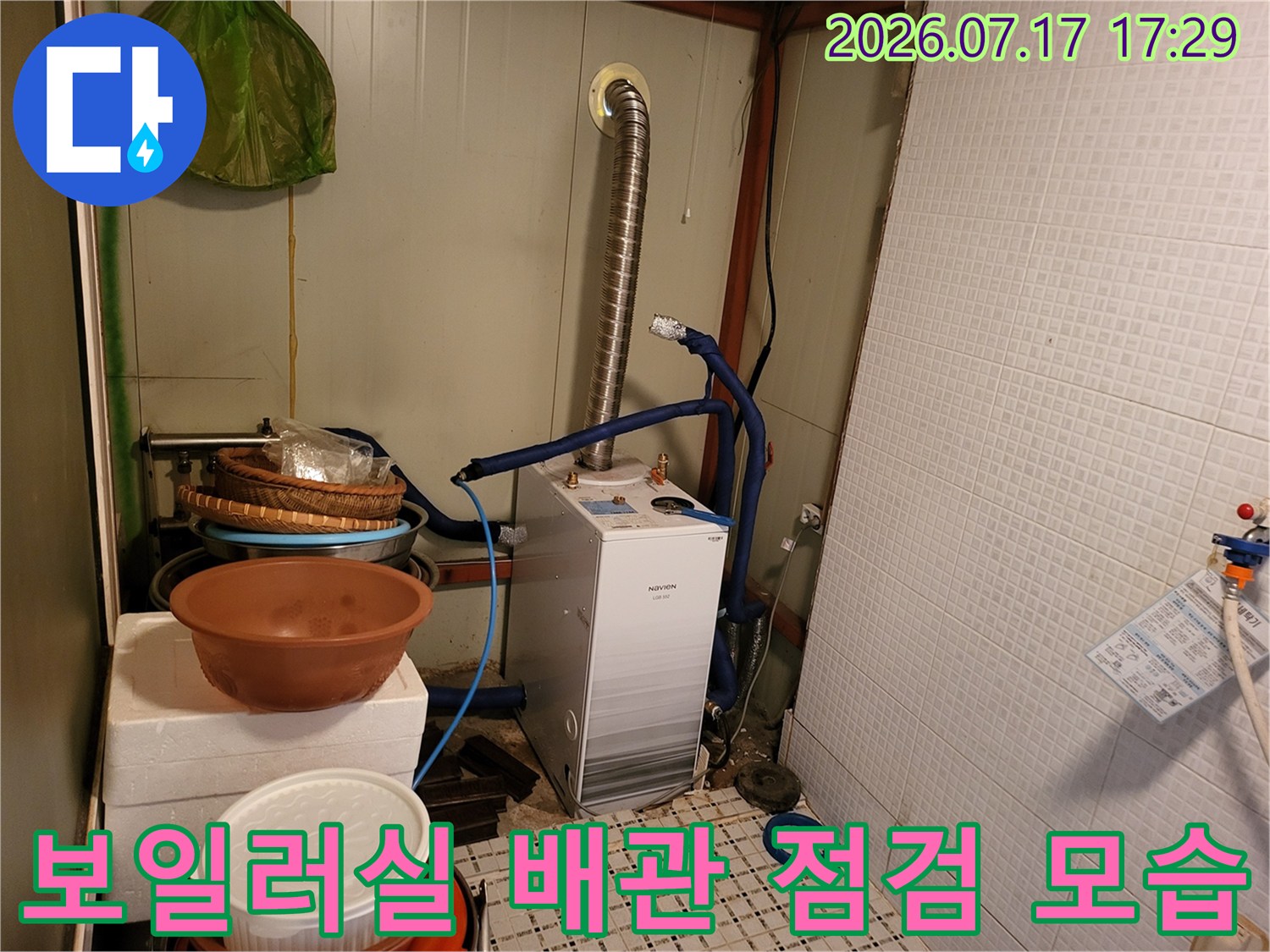 흰색 보일러 본체와 연결된 파란색 배관-금속 자재들이 배치된 모습