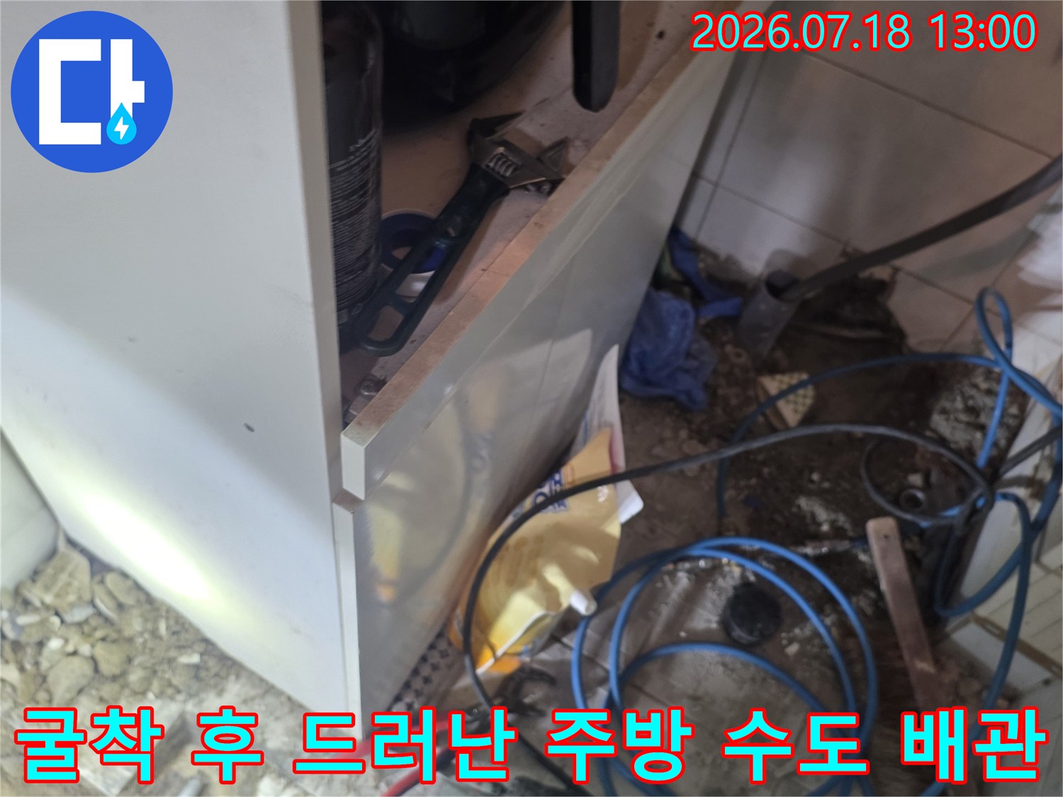 싱크대 하단부의 타일을 제거하고 흙과 모래 사이로 파란색 배관이 노출된 모습