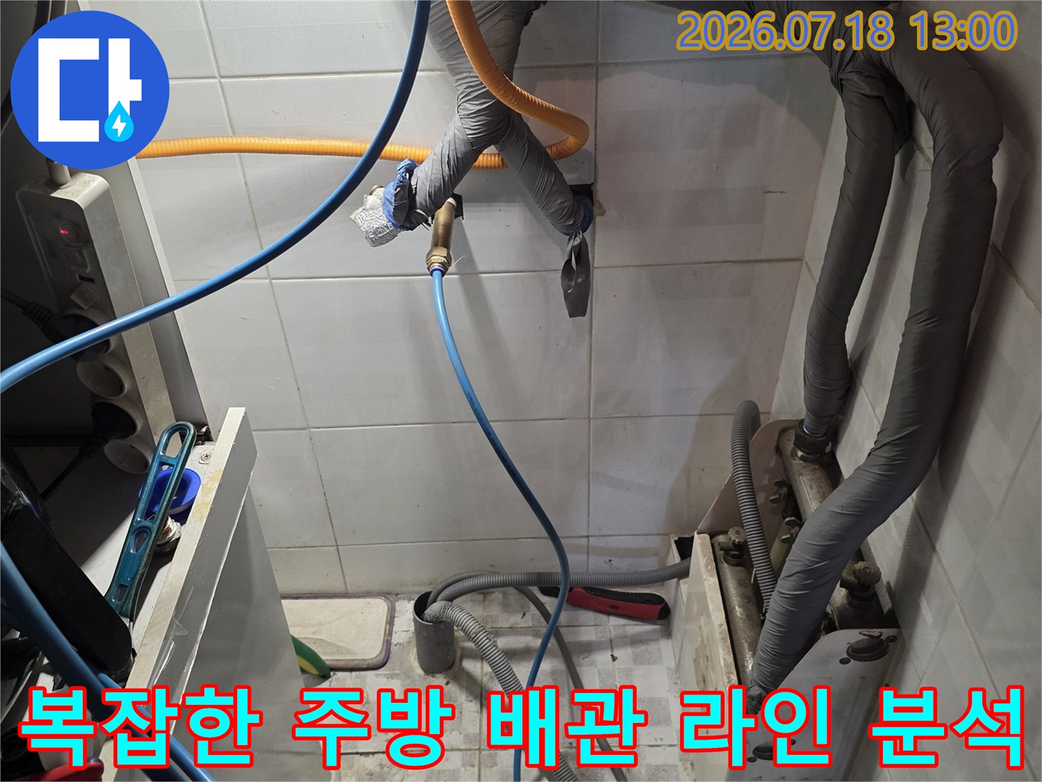 흰색 타일 배경의 복잡한 회색 배관망과 파란색 및 노란색 호스가 연결된 모습-누수 탐지 현장