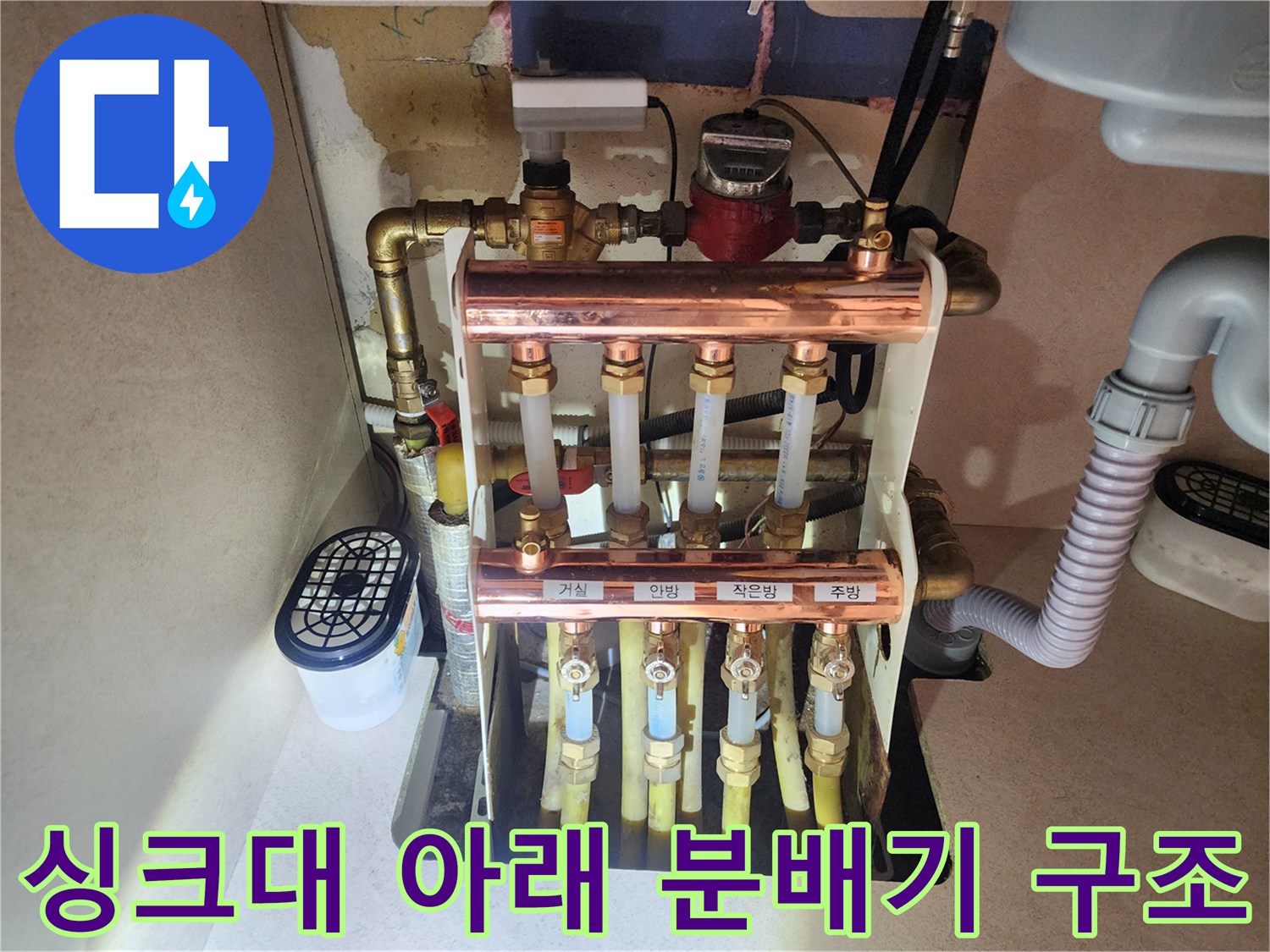싱크대 하부장 내부에 설치된 난방 분배기와 연결된 여러 개의 밸브와 배관들
