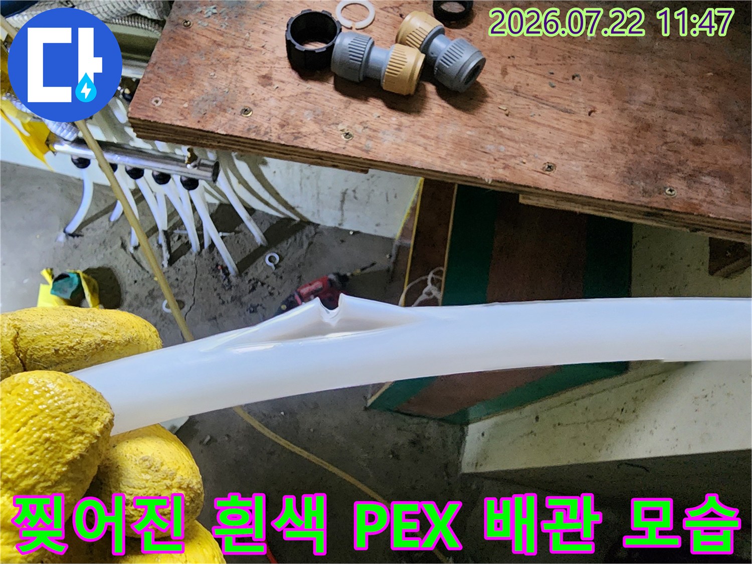 노란색 작업 장갑을 낀 손으로 파손되어 찢어진 흰색 보일러 배관 부위를 들어 올린 모습