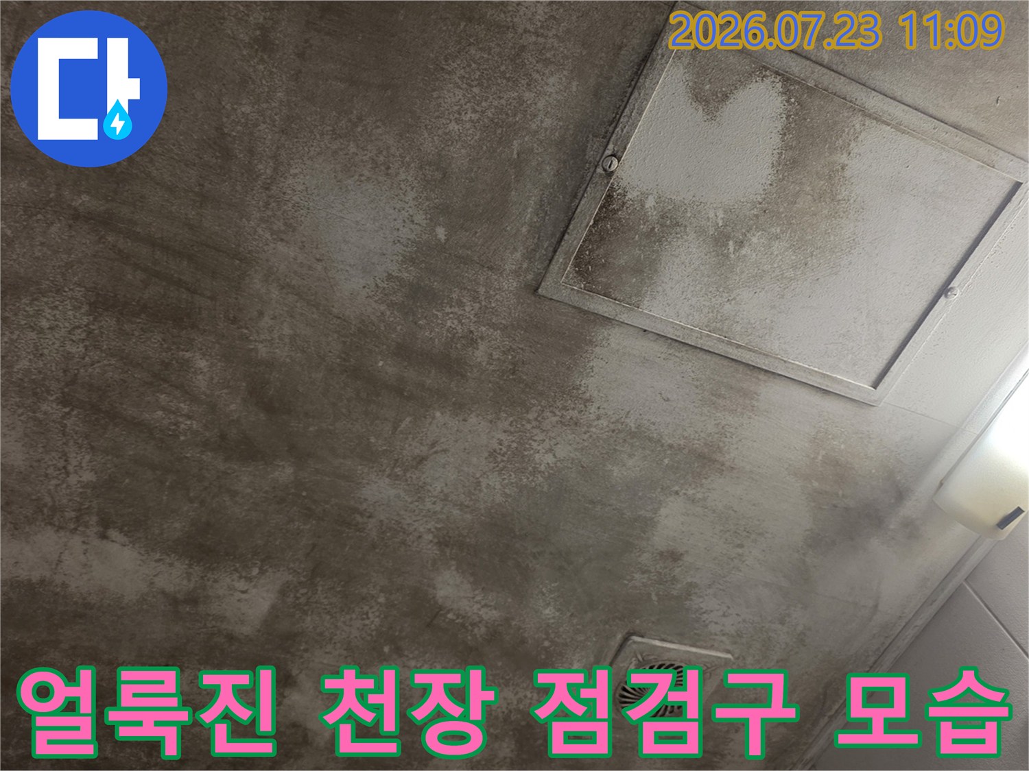 회색빛 천장에 물자국 얼룩이 넓게 퍼져 있고 사각형 점검구가 설치된 모습