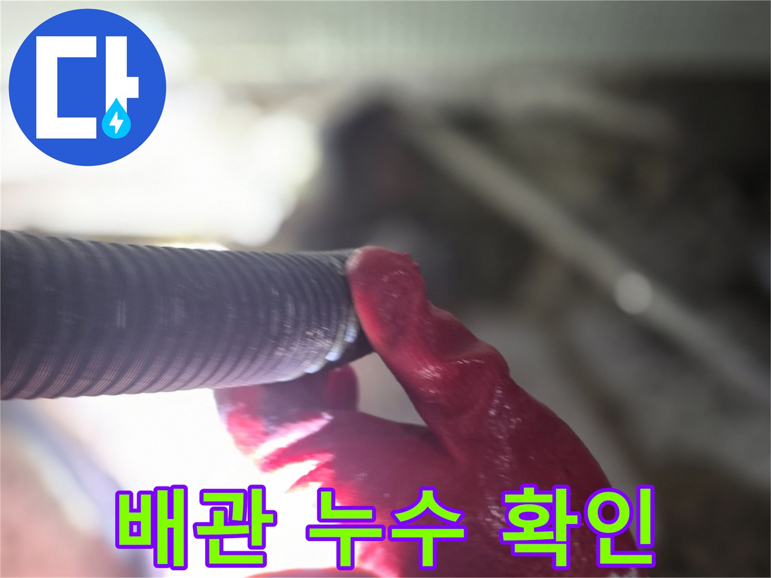 붉은색 장갑을 낀 작업자가 배관의 연결 부위를 손으로 만지며 상태를 점검하고 있습니다.