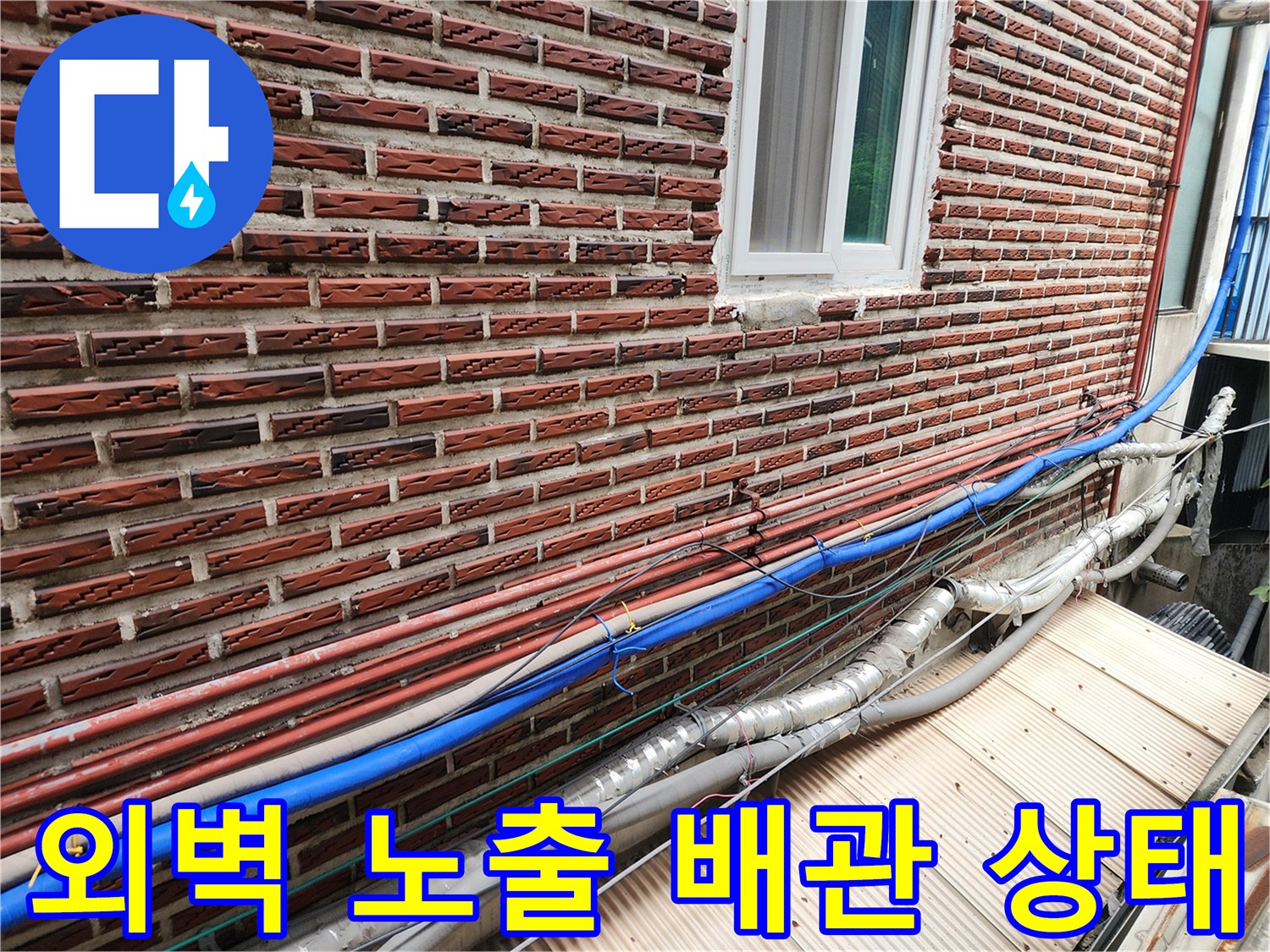 붉은 벽돌 외벽에 설치된 파란색과 붉은색 배관들-노후된 보온재 상태를 보여줌