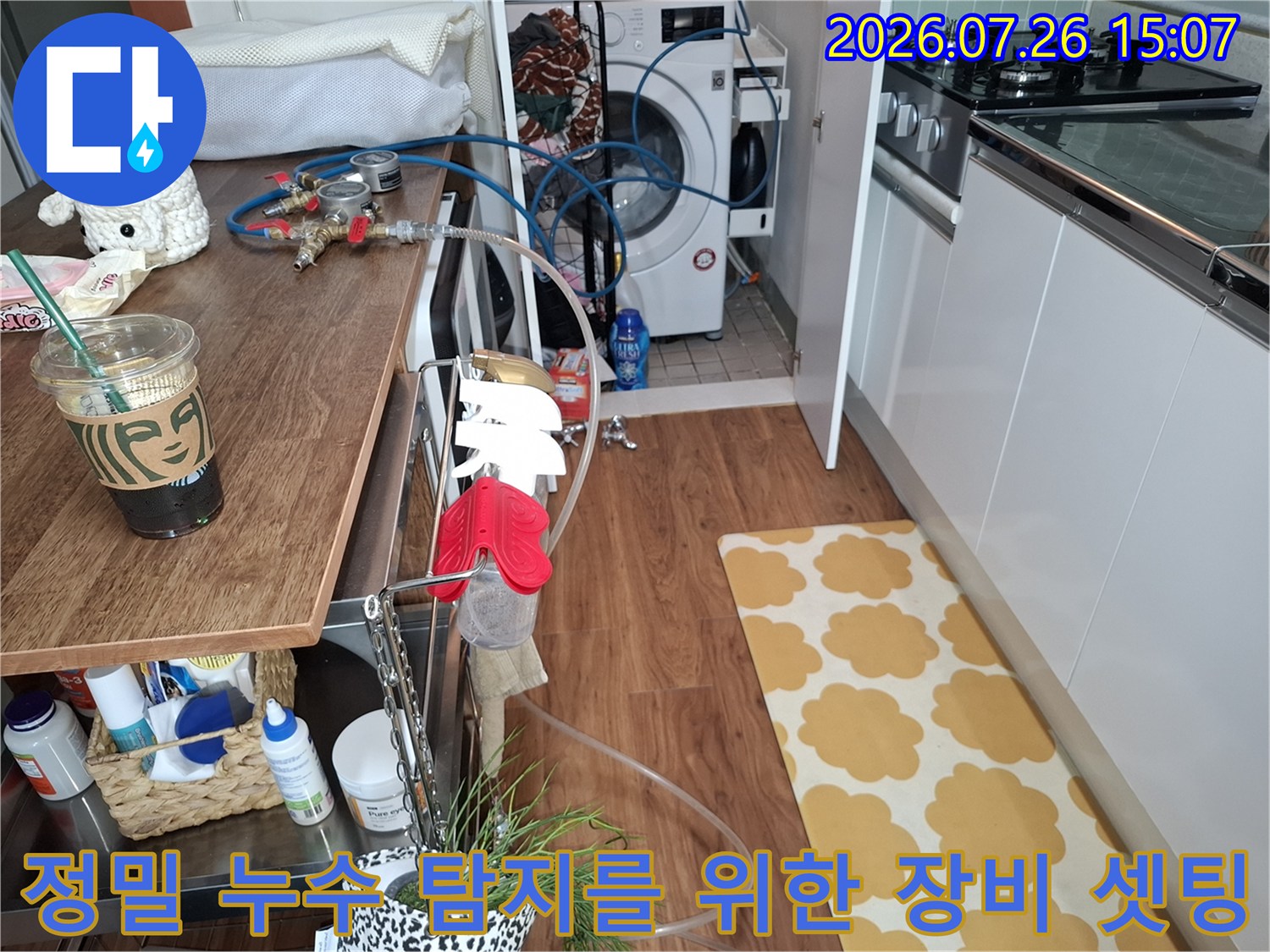 주방 가구와 세탁기 사이 공간에 설치된 파란색 배관 테스트 호스와 측정 장치-누수 원인 규명을 위한 진단 장면