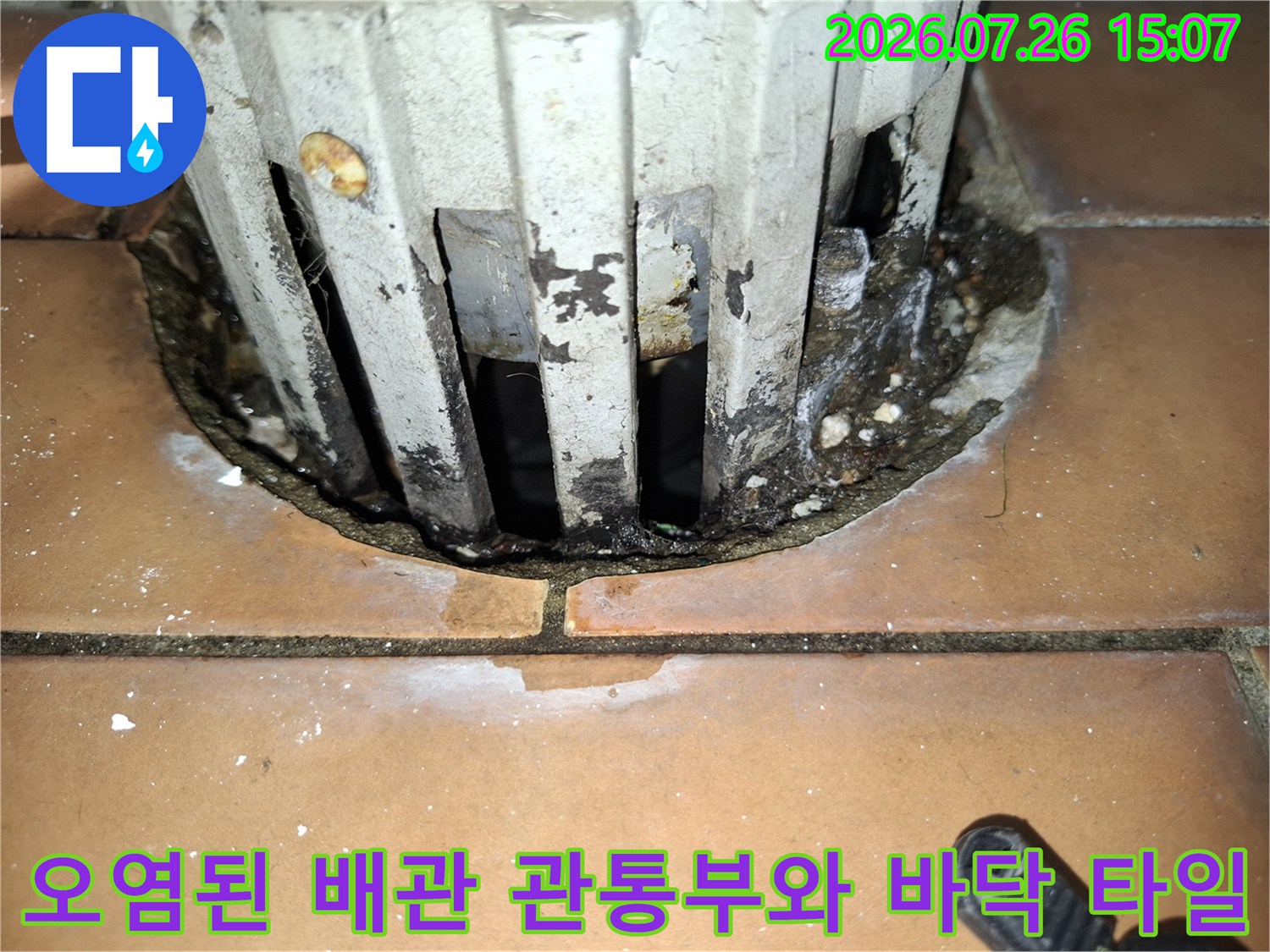흰색 배관의 수직 홈 부분에 검은 오염물이 묻어 있고 바닥 접합부가 벌어진 사진