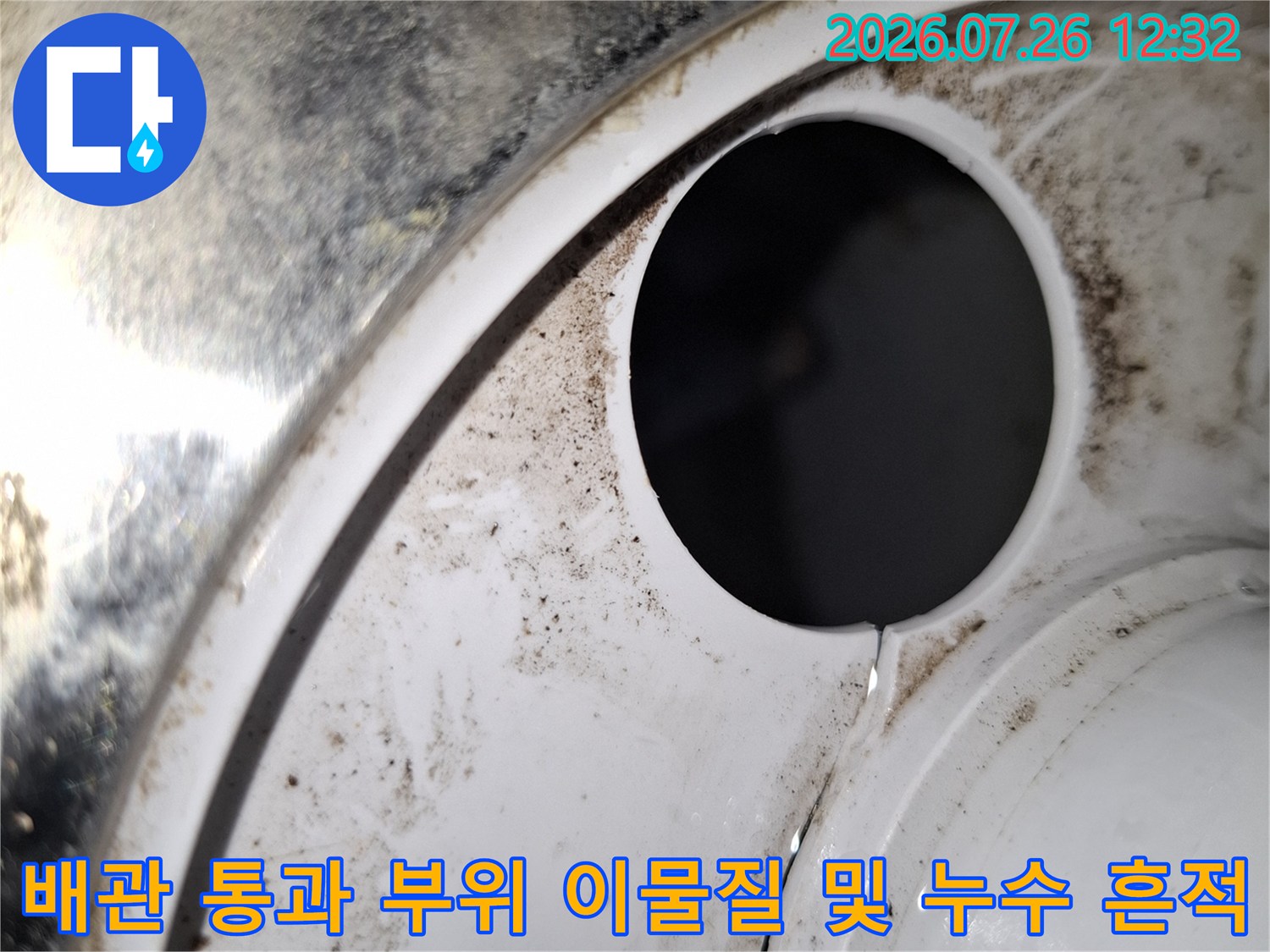 원형 배관 구멍 주변의 흰색 마감재에 묻은 검은색 물때와 오염-누수의 직접적인 증거입니다.