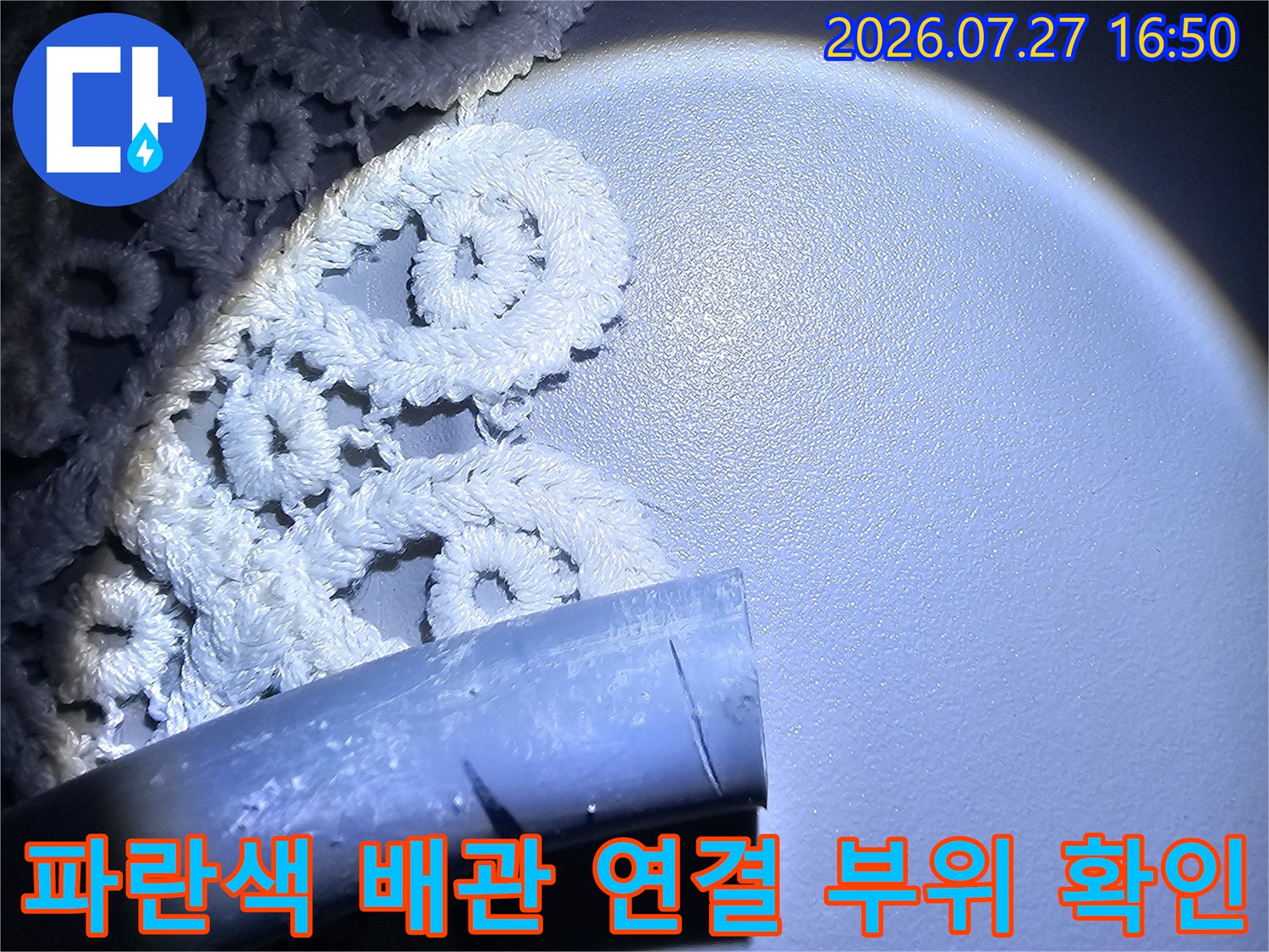 밝은 조명 아래 노출된 화장실 천장의 파란색 플라스틱 배관 단면과 주변 모습