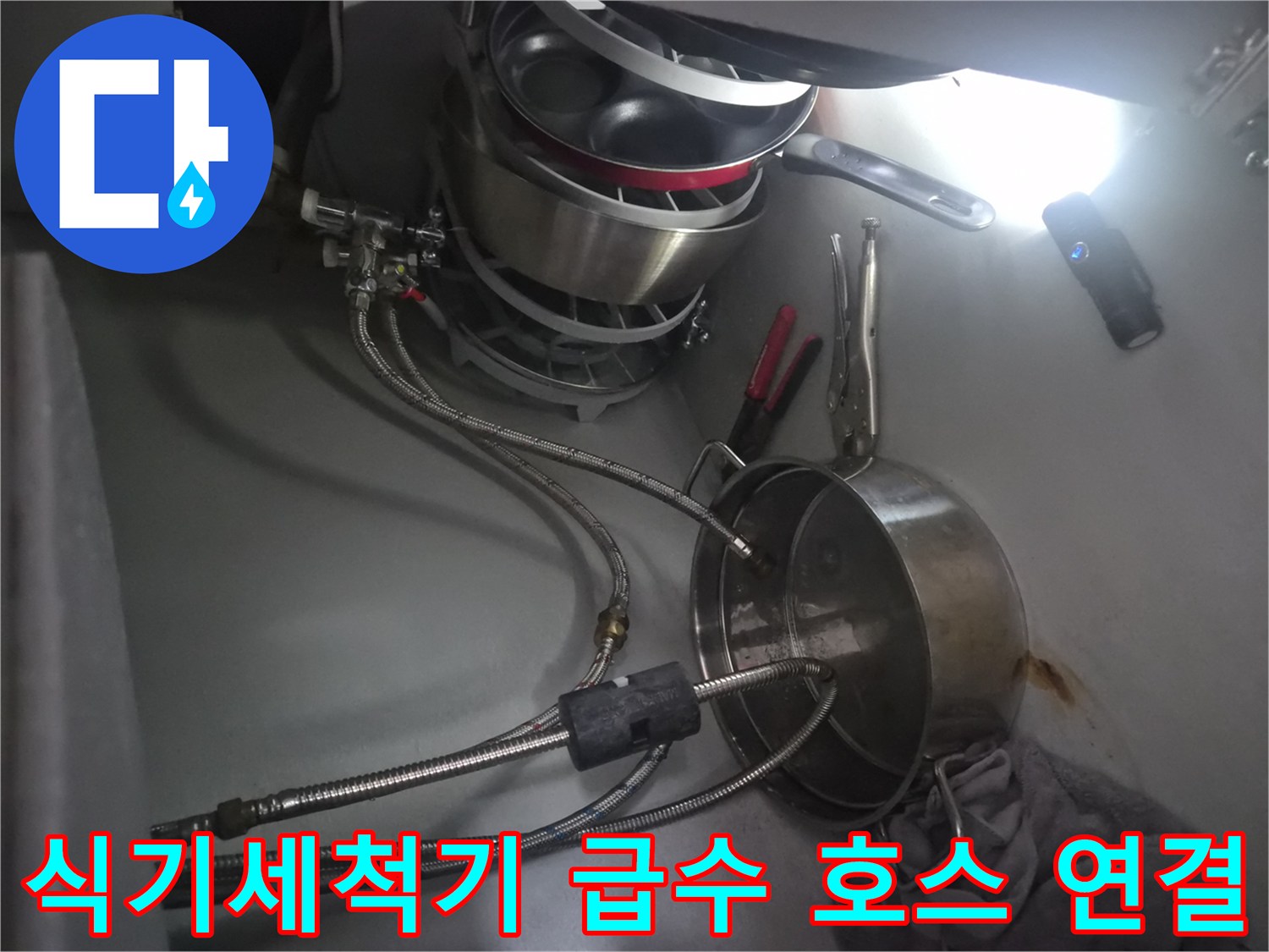싱크대 밑에 놓인 냄비와 식기세척기용 금속 배관의 모습